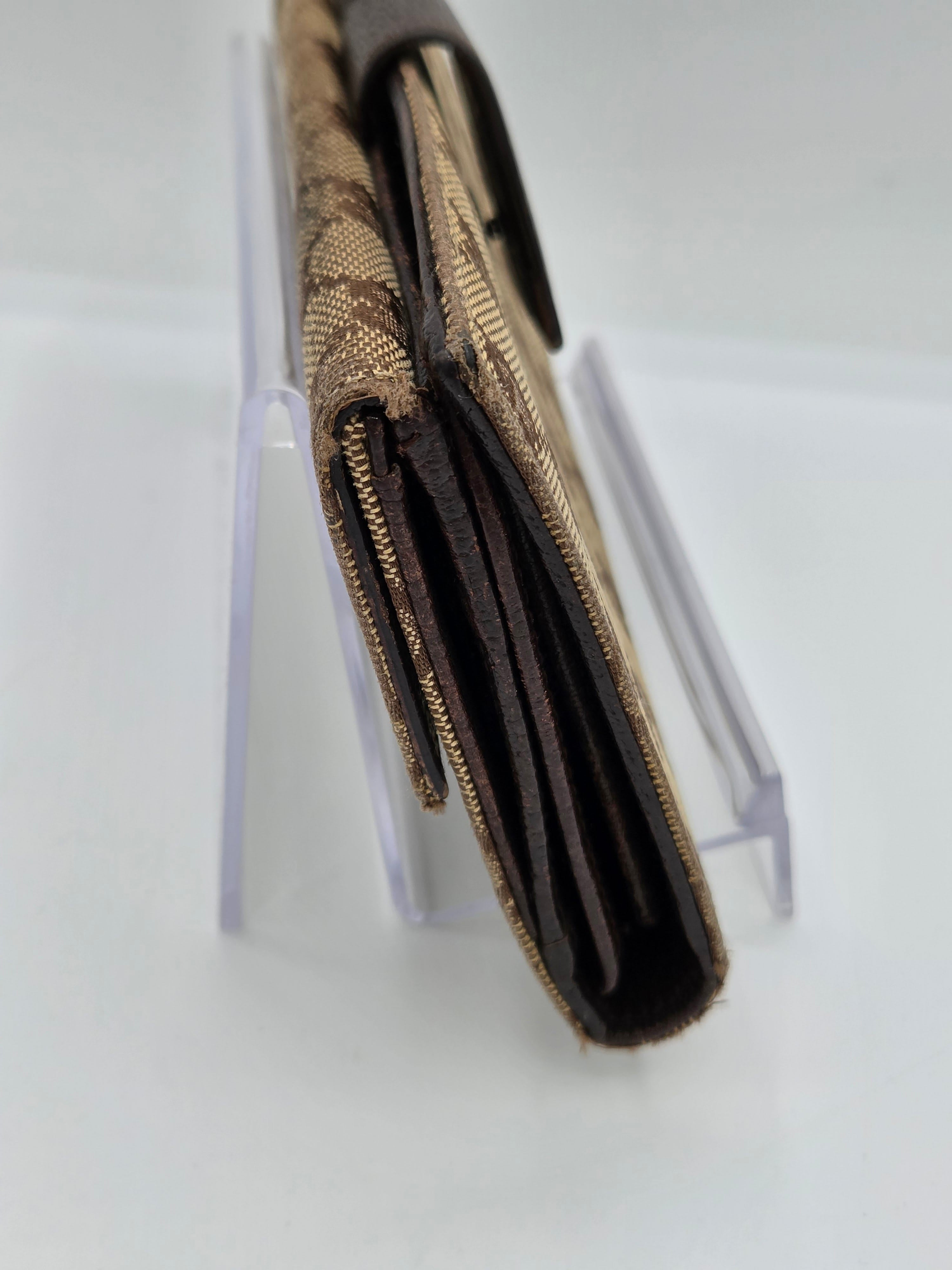 A close-up of a brown and beige patterned wallet or card holder with dark brown interior lining, displayed on a clear acrylic stand against a white background.