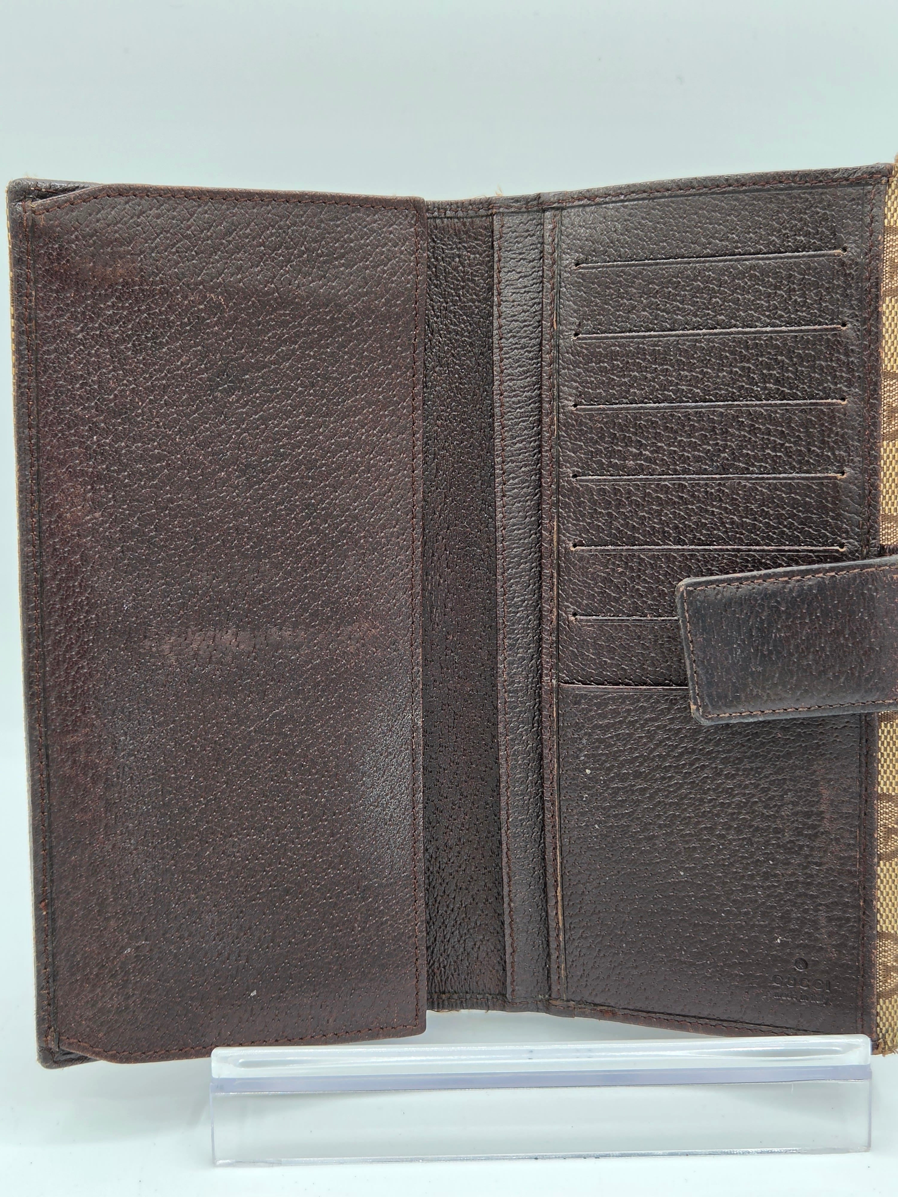 A dark brown textured leather wallet shown open, featuring card slots and a strap closure, photographed against a plain light background.