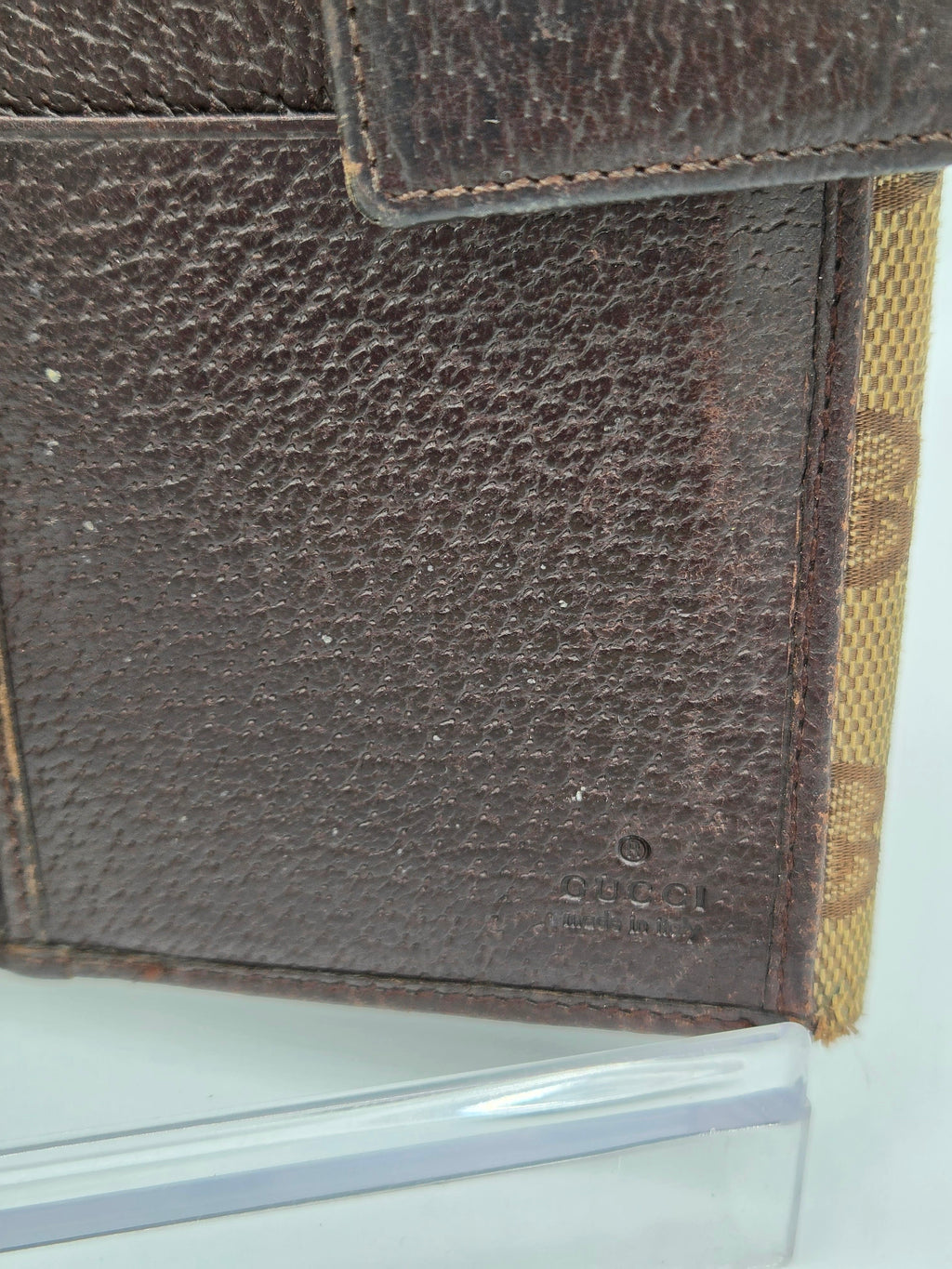 Close-up of a dark brown pebbled leather wallet or card holder with a tan monogram patterned fabric trim along the top edge.
