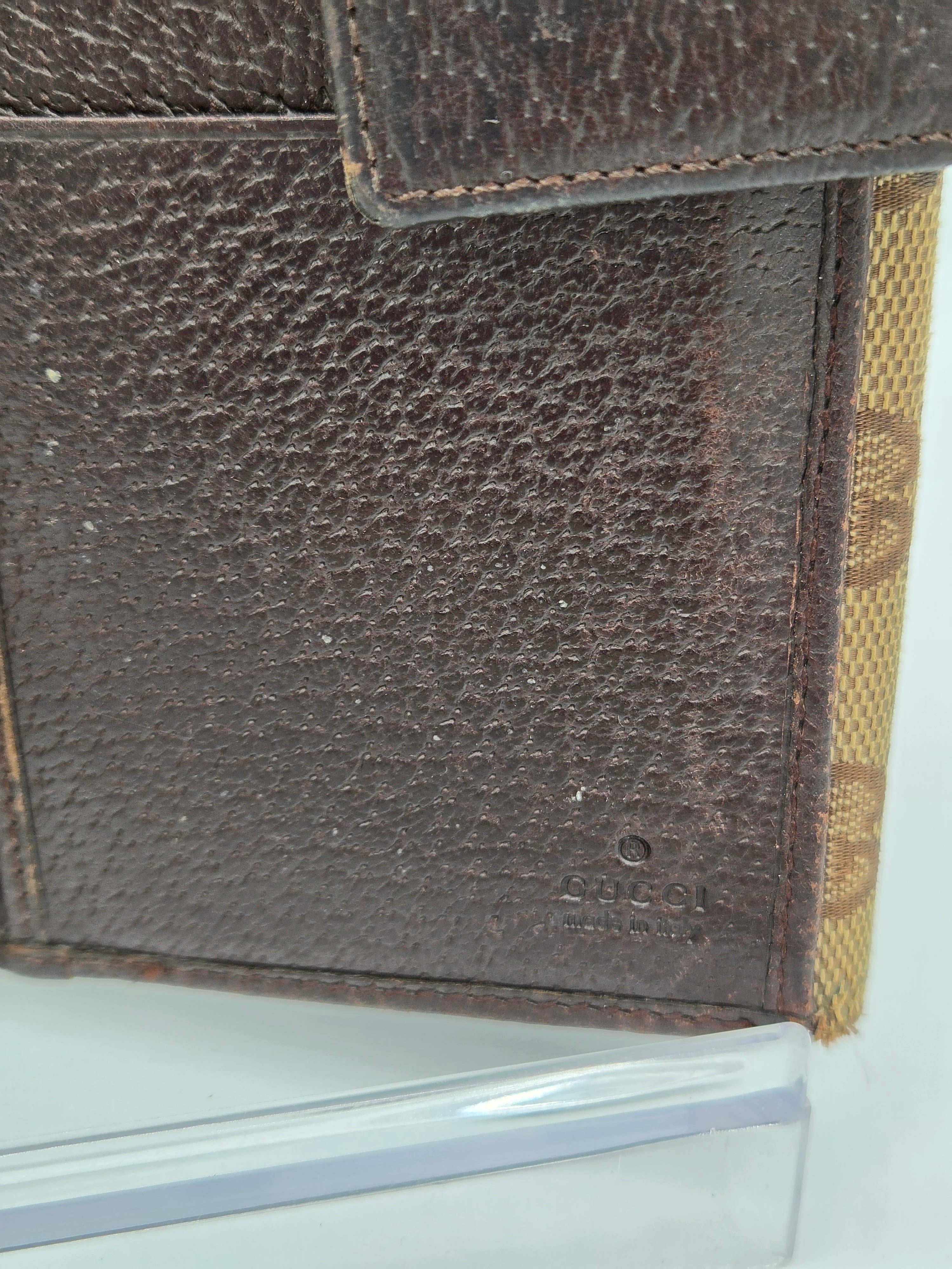 Close-up of a dark brown pebbled leather wallet or card holder with a tan monogram patterned fabric trim along the top edge.