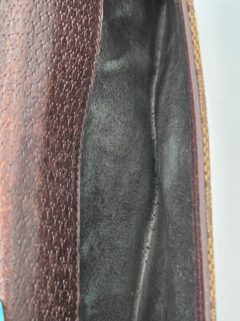 Close-up detail of a dark brown textured leather pouch showing the interior lining and a gold-toned stitched edge.