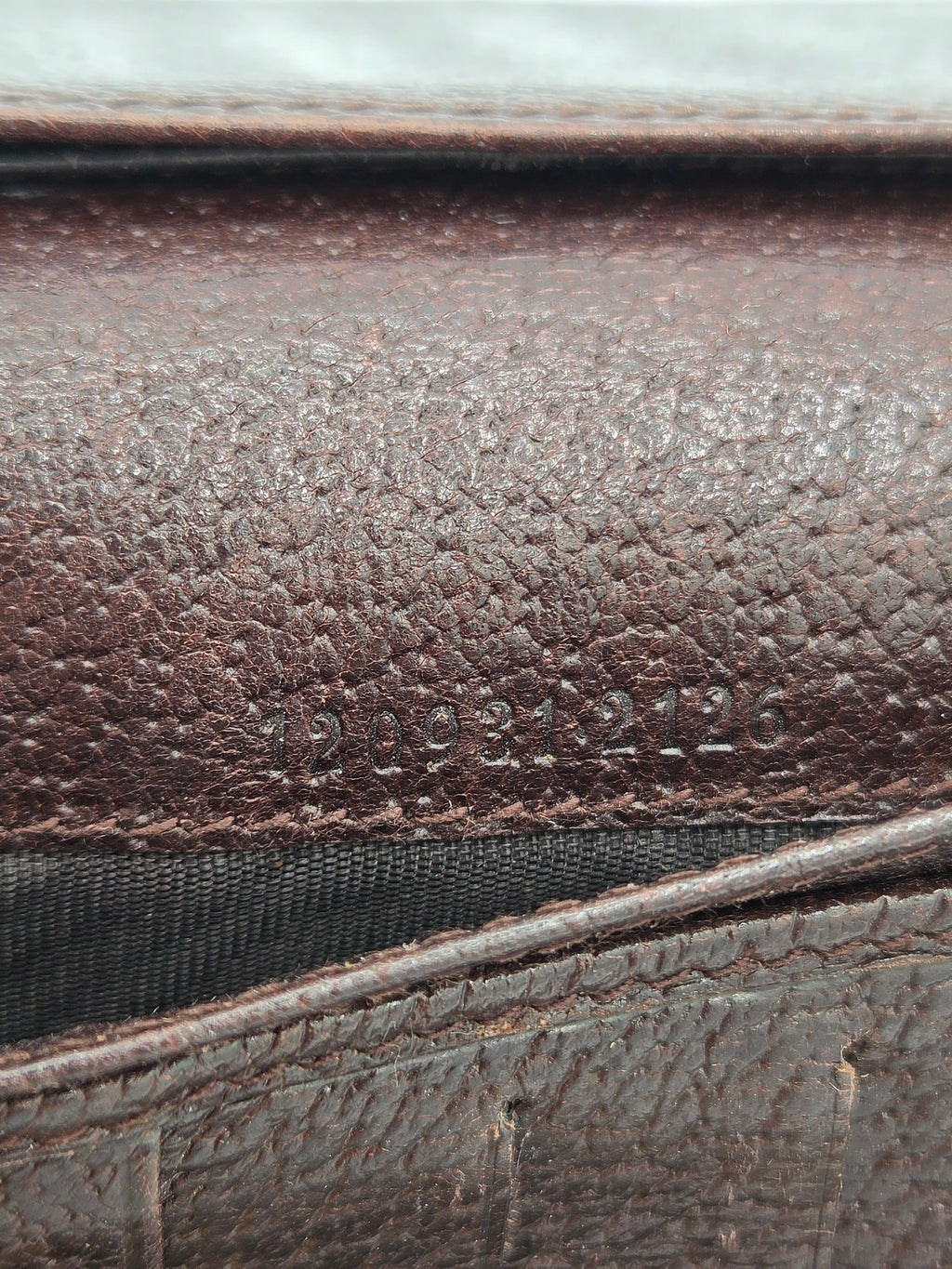 Close-up of a dark brown textured leather surface with visible grain, stitching, and a black mesh-like material along the side.