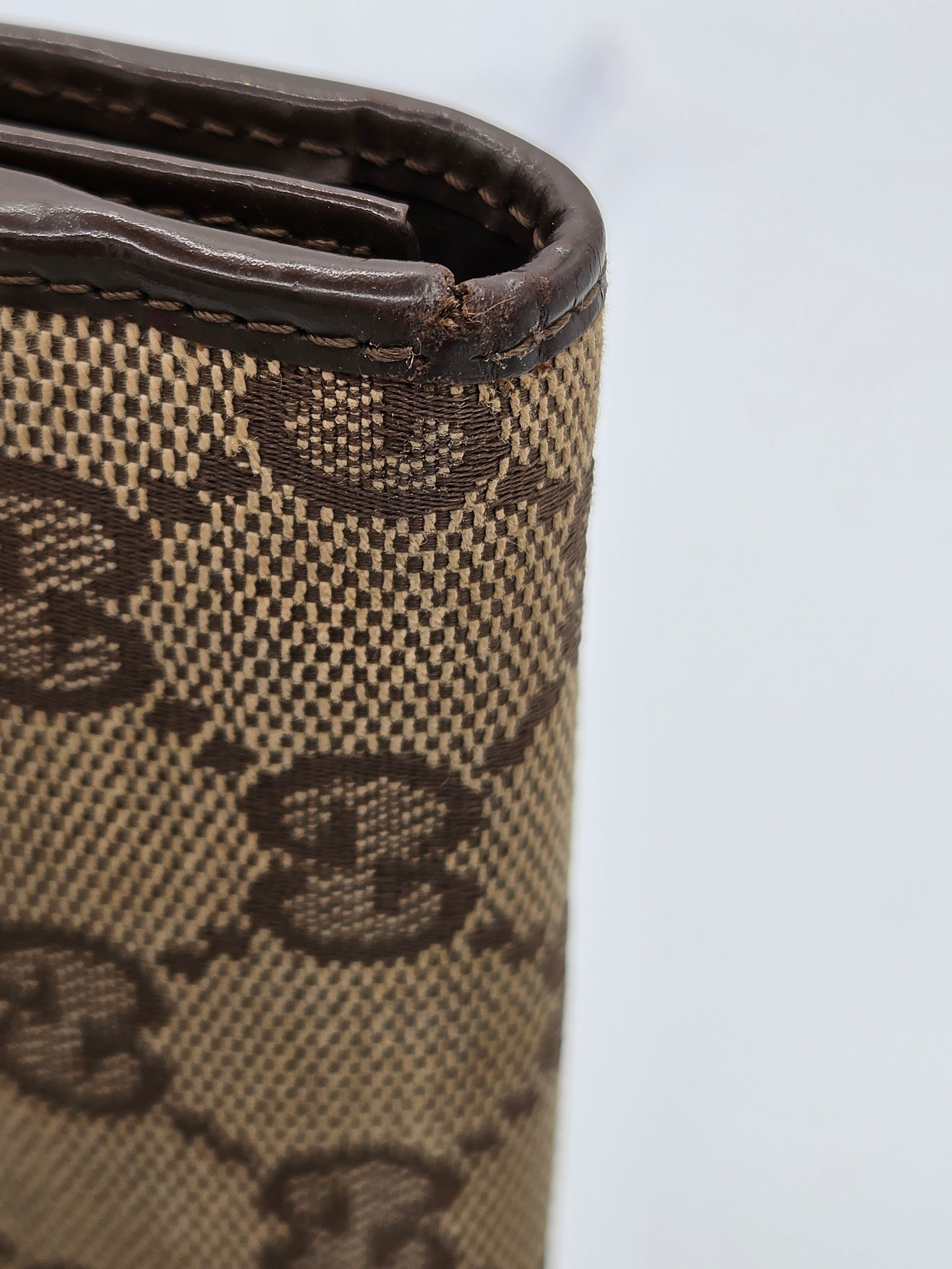 Close-up of a Gucci wallet in the classic GG Supreme canvas, showing the beige and brown monogram pattern and dark brown leather trim.