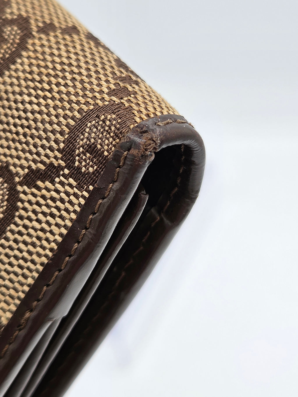 Close-up of a brown and beige patterned wallet corner with dark brown leather trim and stitching, on a light gray background.