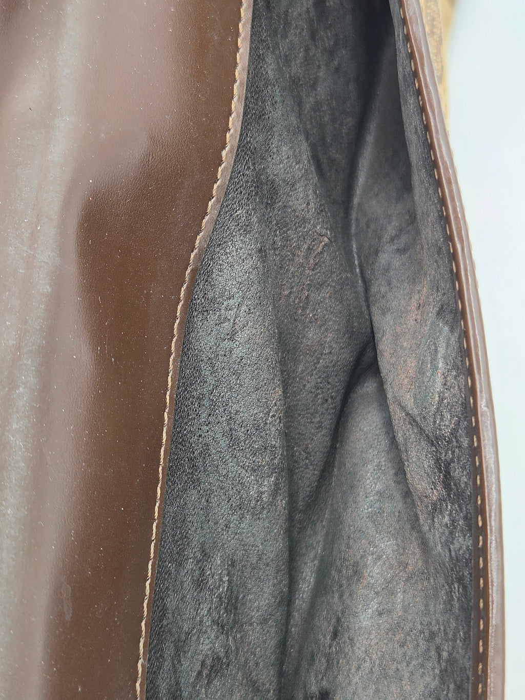 Close-up of the interior lining of a brown leather bag, showing a dark gray suede or microfiber fabric lining with visible stitching along the edge.