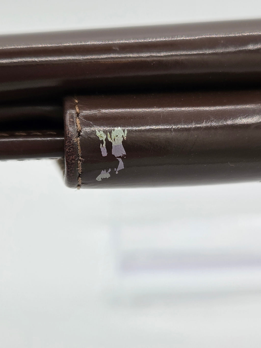 Close-up of a dark brown leather chair leg with a worn, chipped section showing the off-white base material underneath.