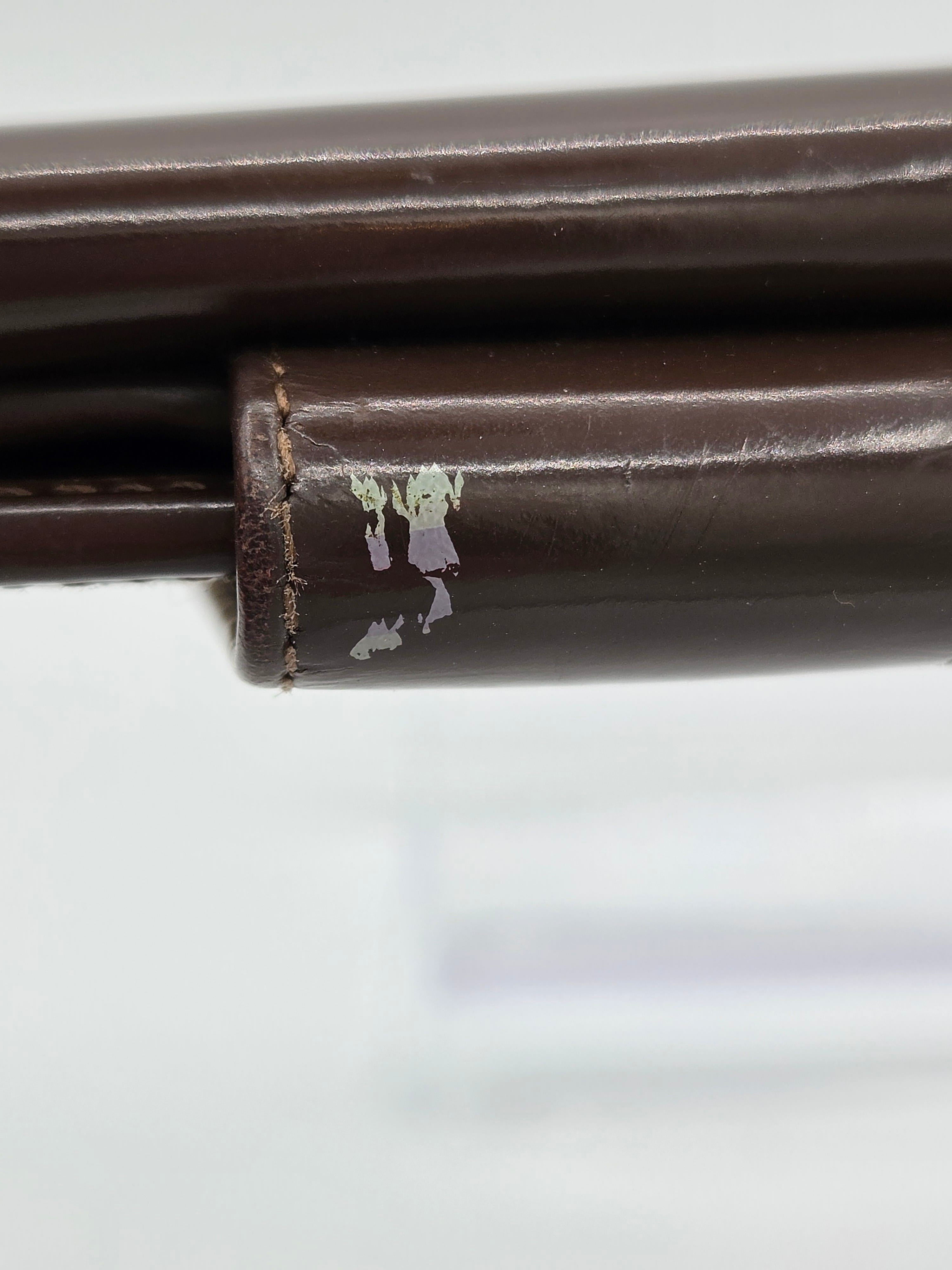 Close-up of a dark brown leather chair leg with a worn, chipped section showing the off-white base material underneath.