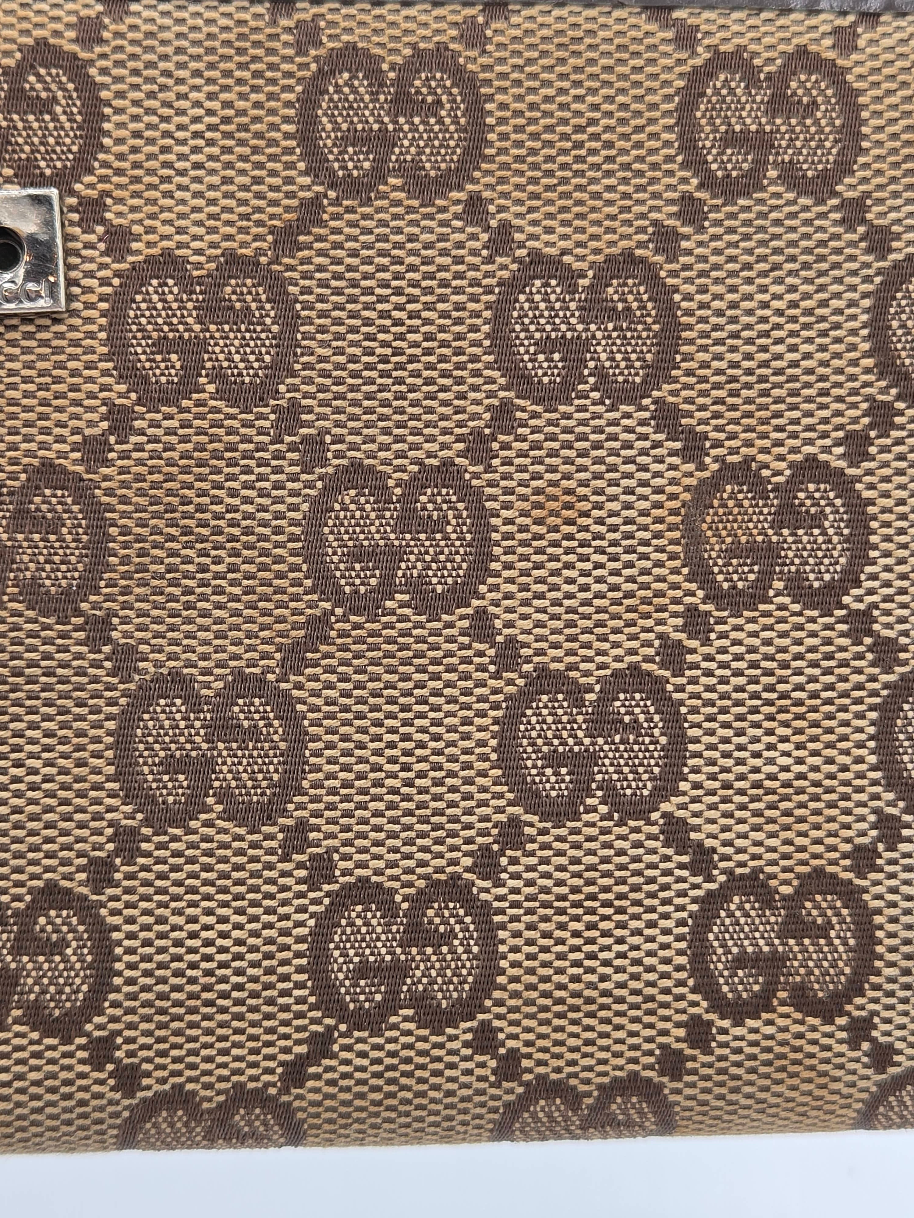 Close-up of a beige and brown monogram patterned material with repeating interlocking GG motifs, likely coated canvas or fabric.
