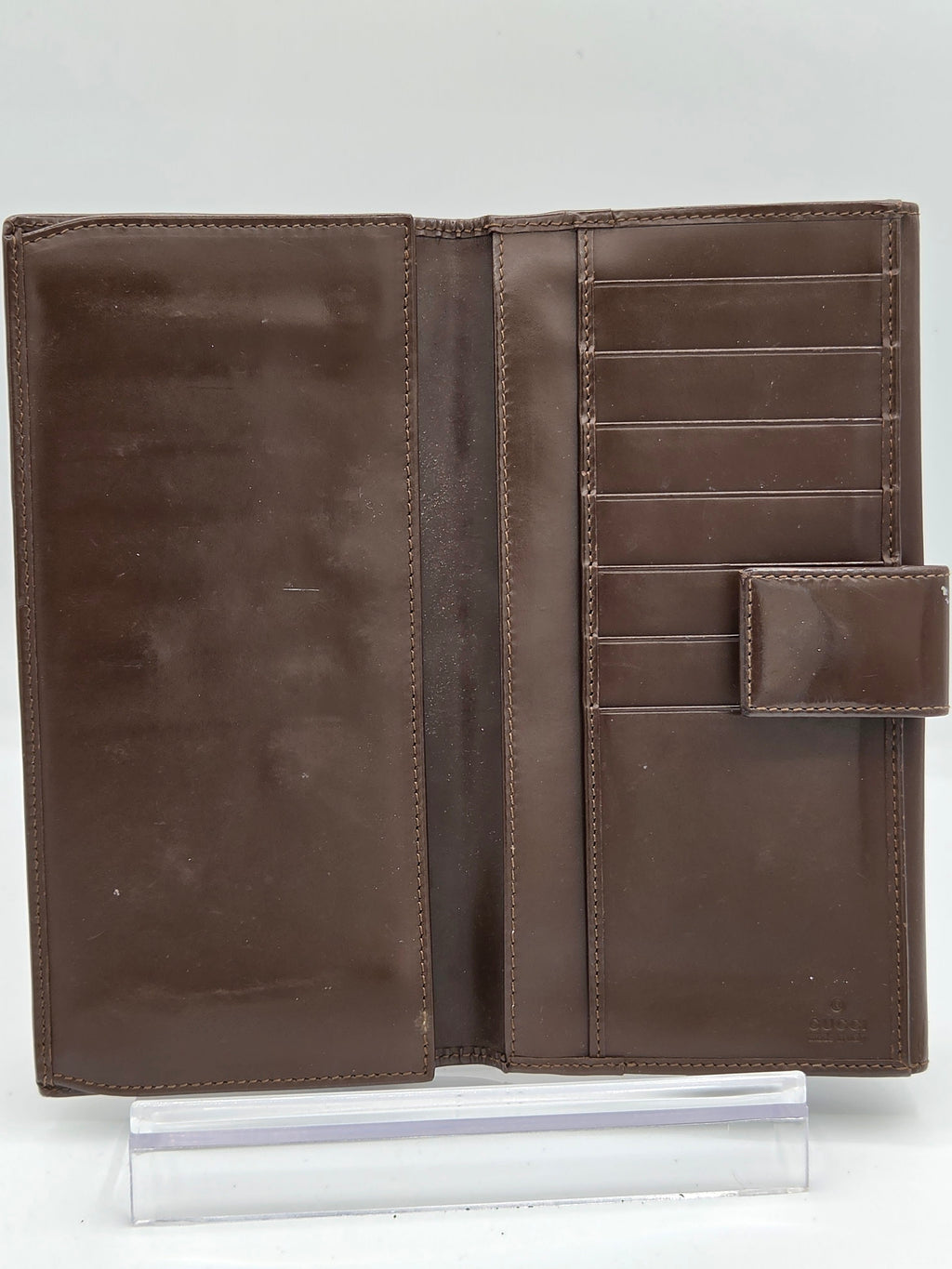 A brown leather wallet shown open, displaying multiple card slots, a central slip pocket, and a top strap closure, photographed on a plain white background.
