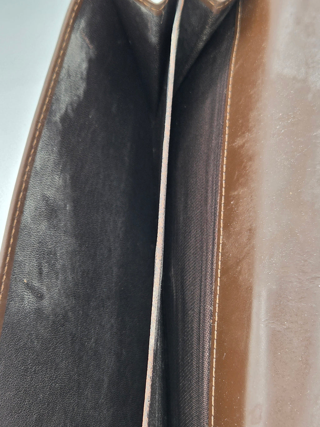 Close-up of the interior of a brown leather clutch or wallet, showing the dark brown fabric lining and a central seam.