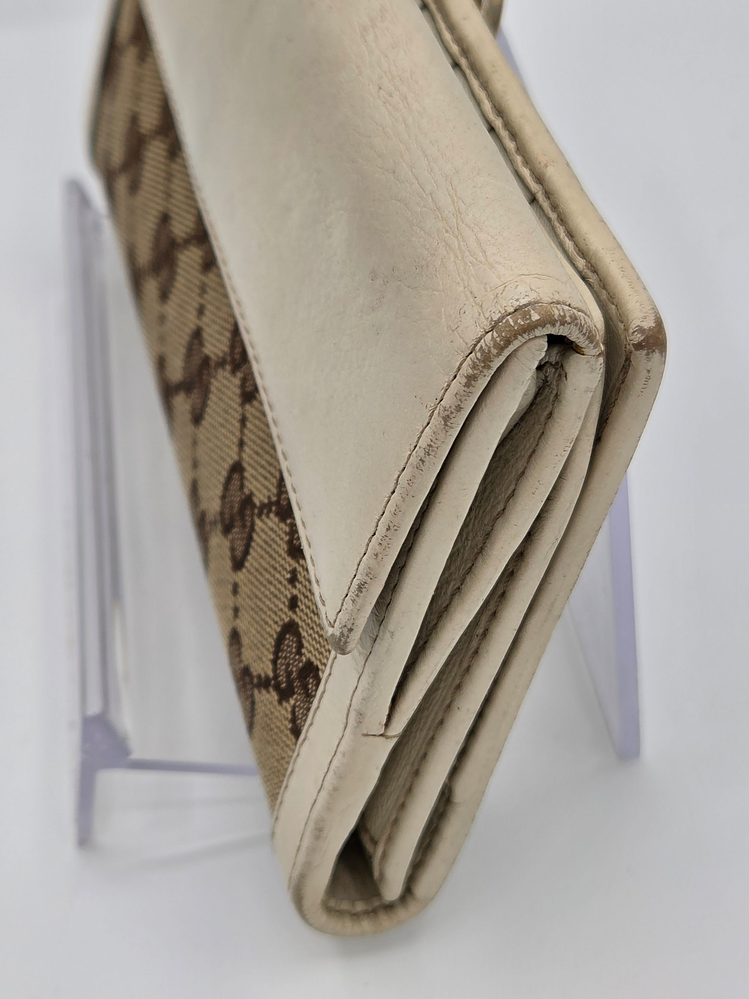 A close-up of a beige leather and brown monogram canvas wallet resting on a clear acrylic display stand against a white background.