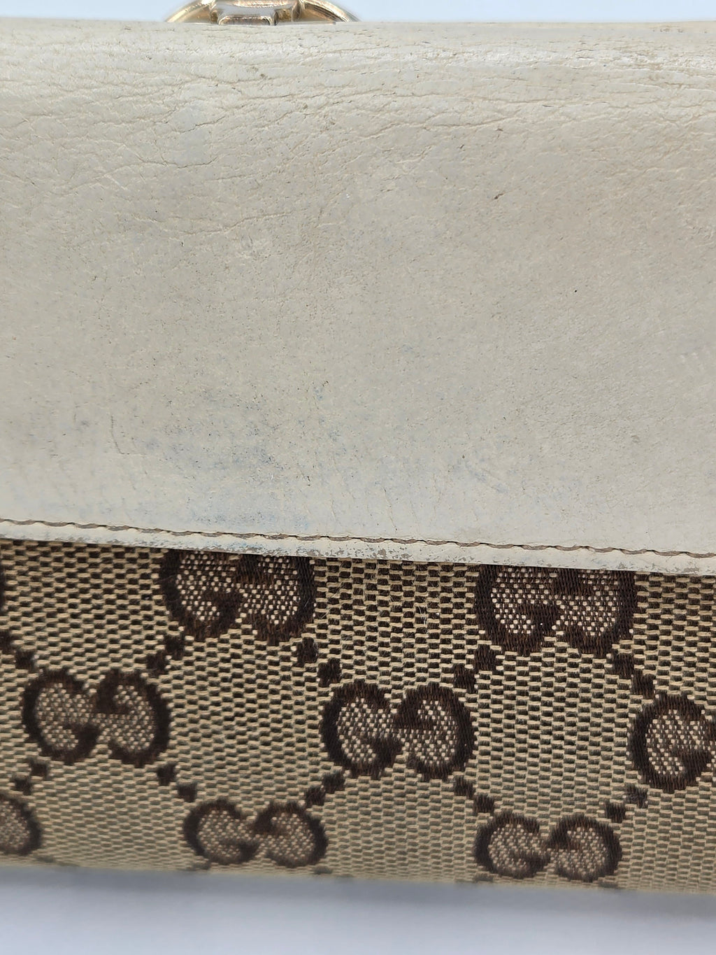 Close-up of a beige and brown monogram canvas bag with a textured off-white leather trim, showing the interlocking GG pattern.