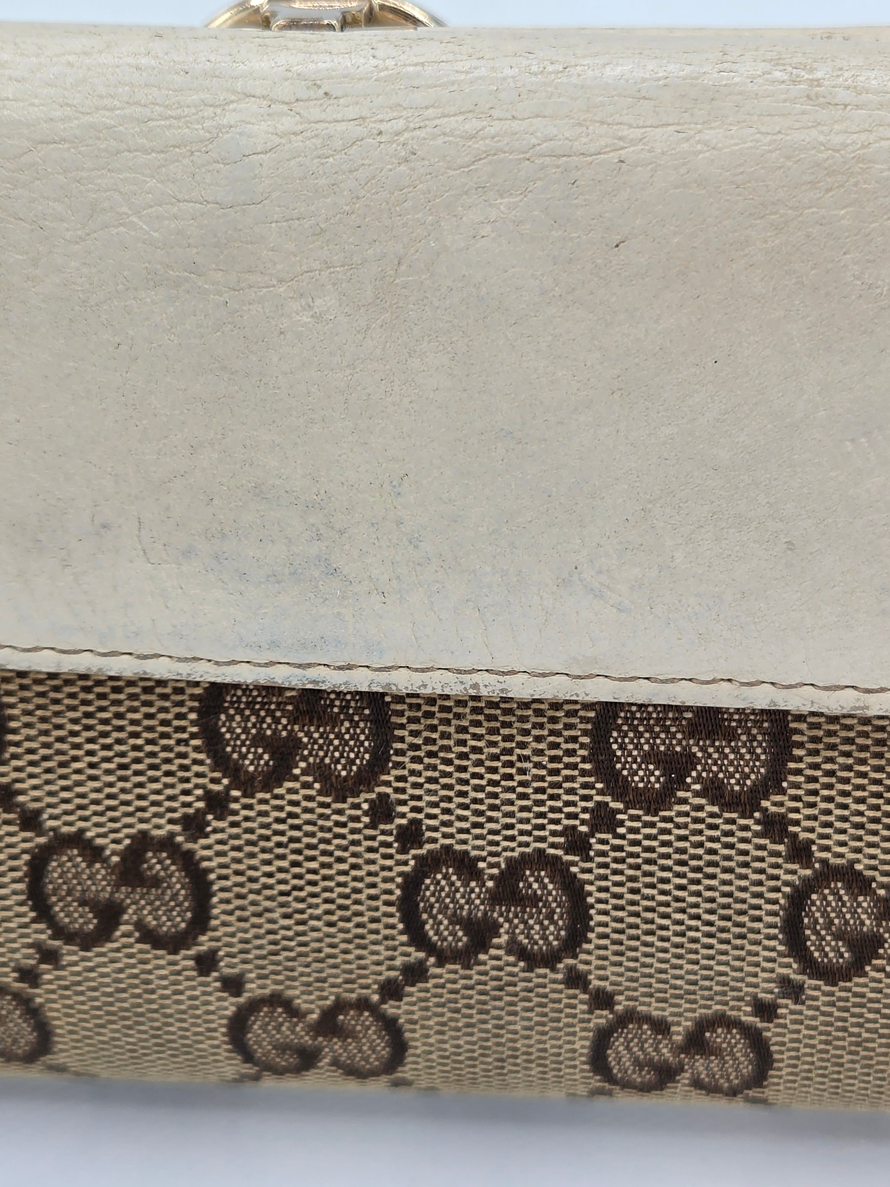Close-up of a beige and brown monogram canvas bag with a textured off-white leather trim, showing the interlocking GG pattern.