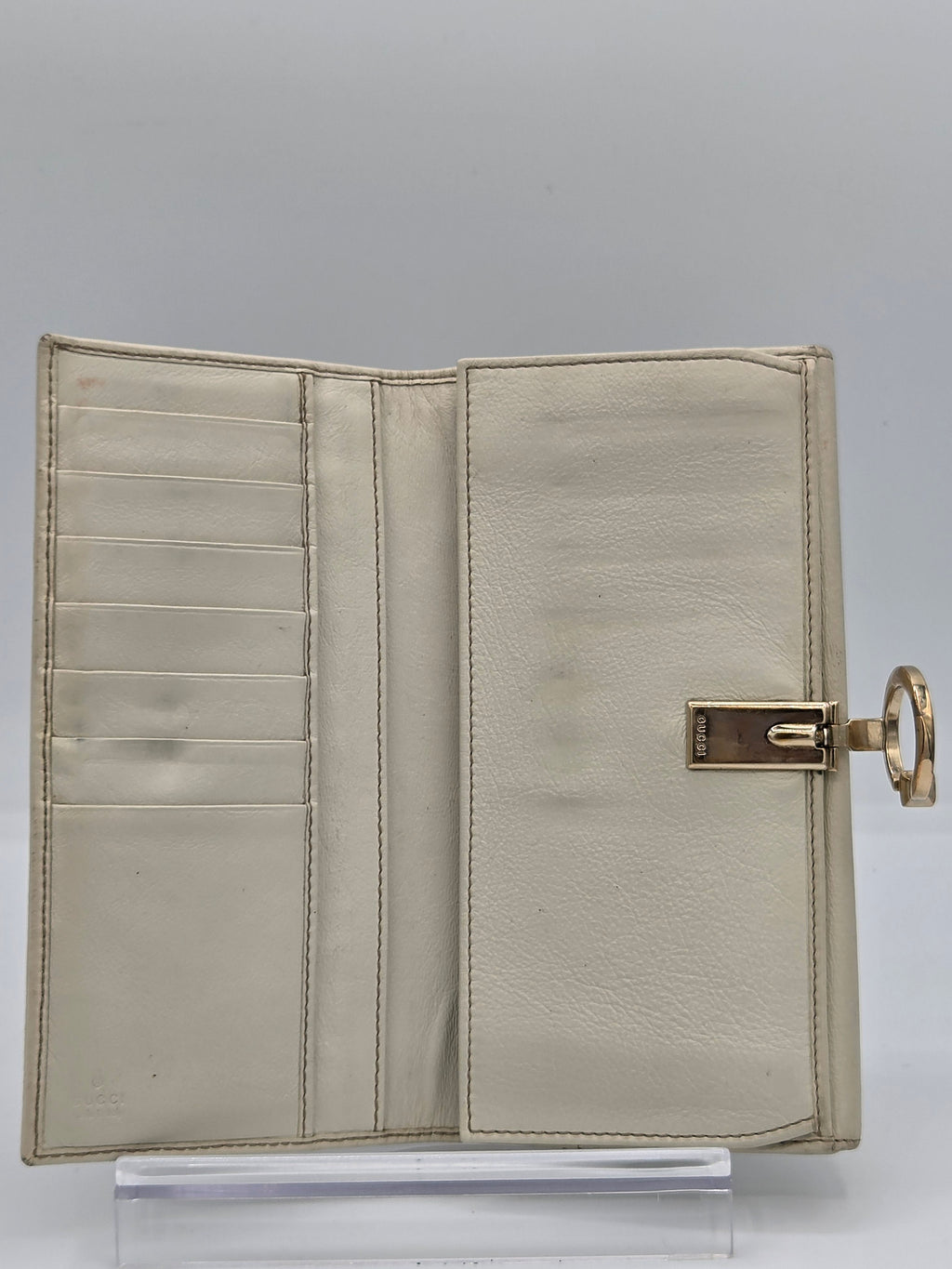 A light beige leather clutch wallet with a gold-tone metal clasp and top ring, shown open to reveal multiple card slots.