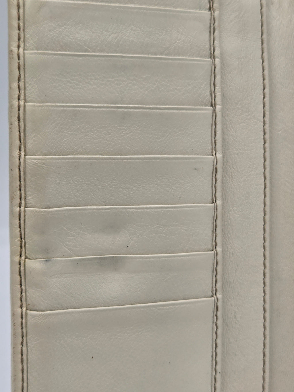 Close-up of a light beige or off-white leather wallet interior showing stitched card slots and a horizontal seam.