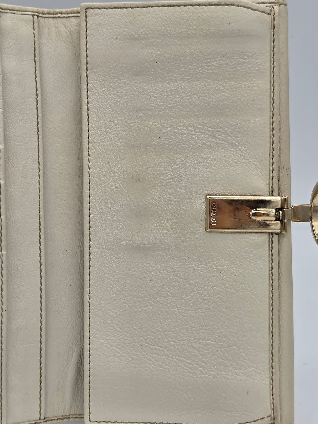 Close-up of a light beige leather wallet showing the interior card slots and a gold-tone metal clasp on the right side.