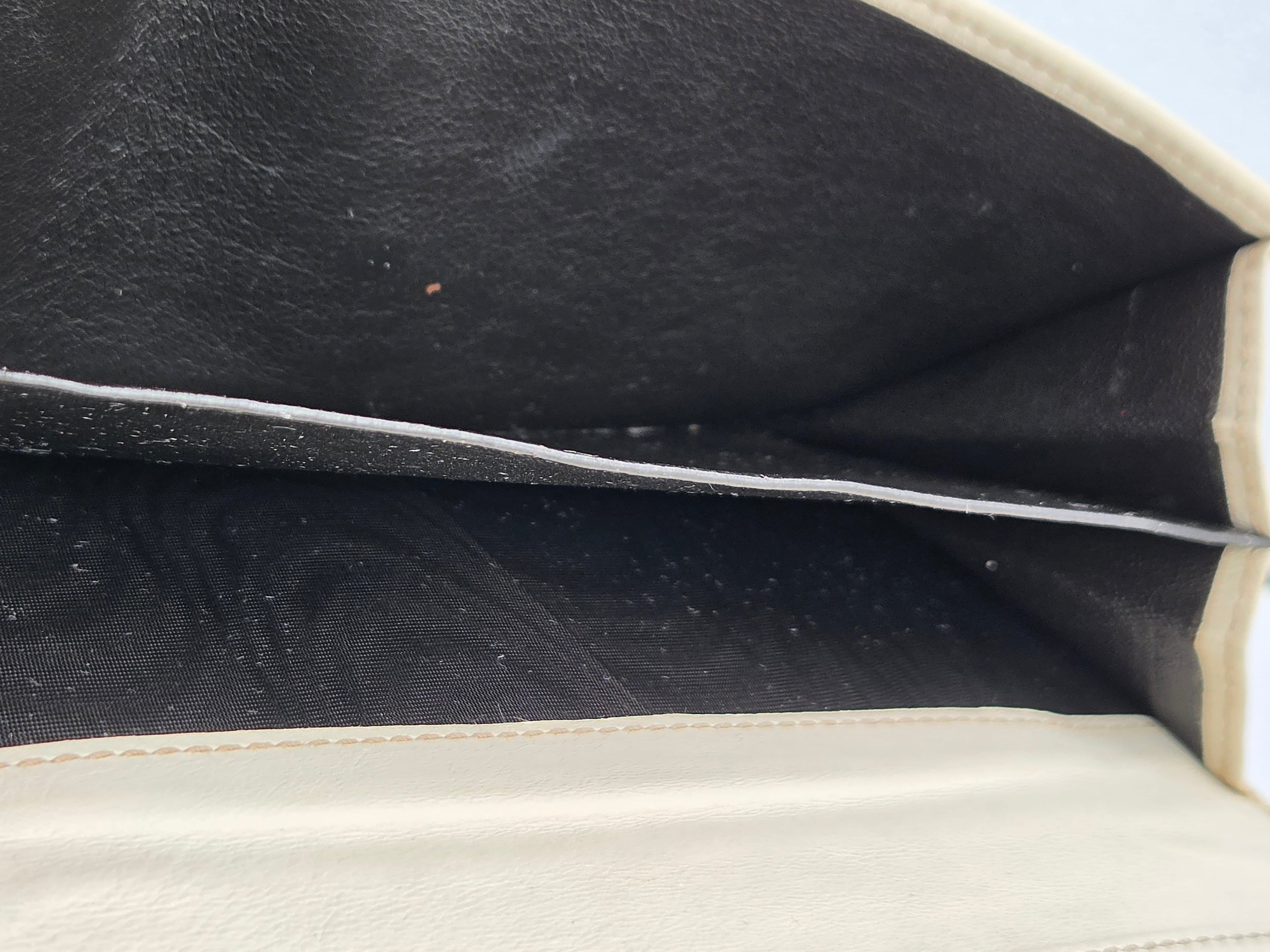 Close-up of the interior of a cream-colored bag, showing a black fabric lining with a horizontal seam running across it.