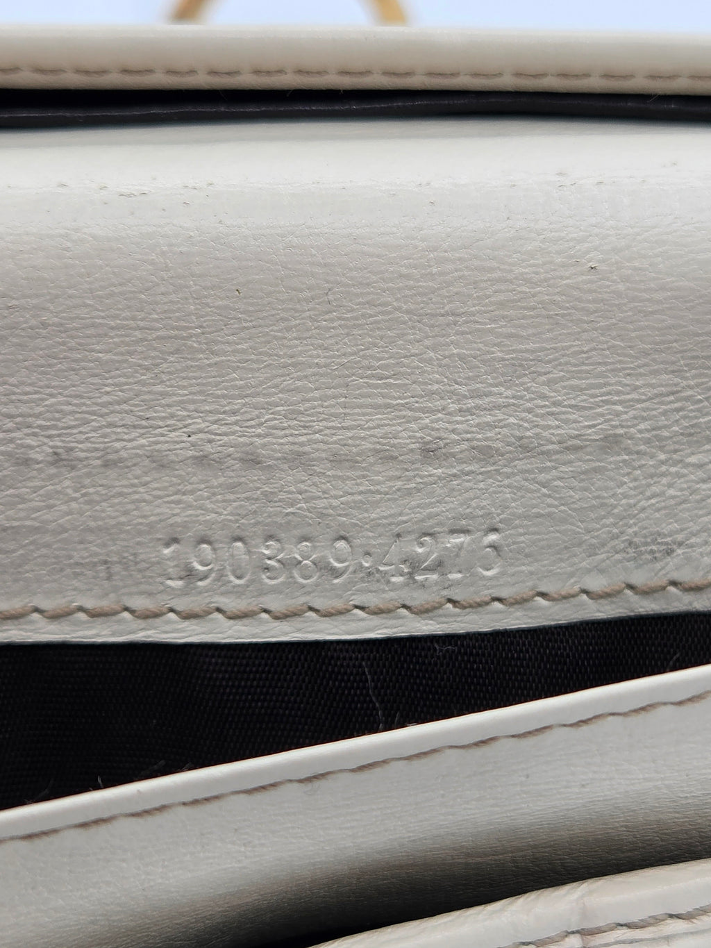 Close-up of a white textured leather wallet or clutch showing the interior black lining and a stamped serial number.