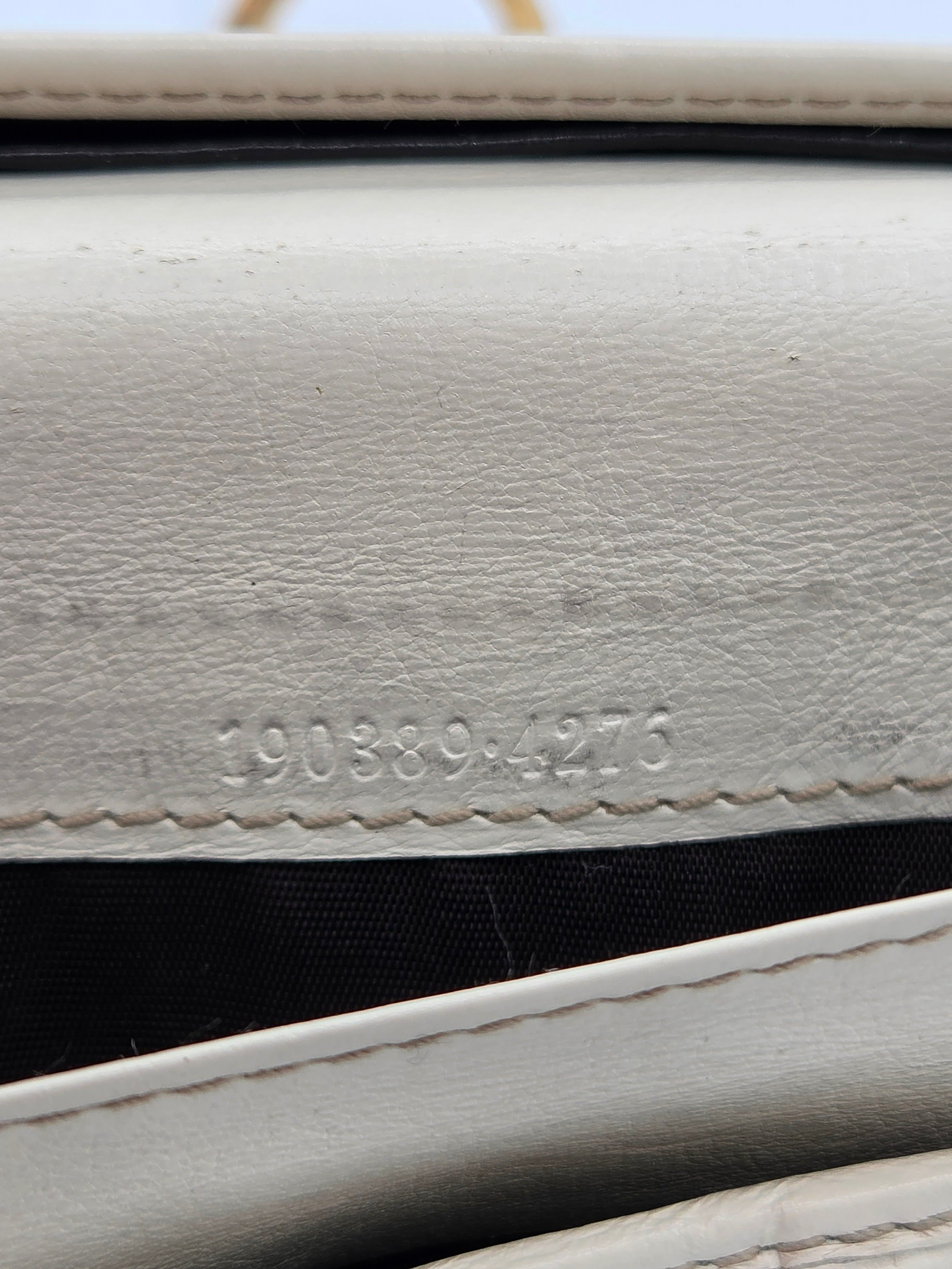 Close-up of a white textured leather wallet or clutch showing the interior black lining and a stamped serial number.