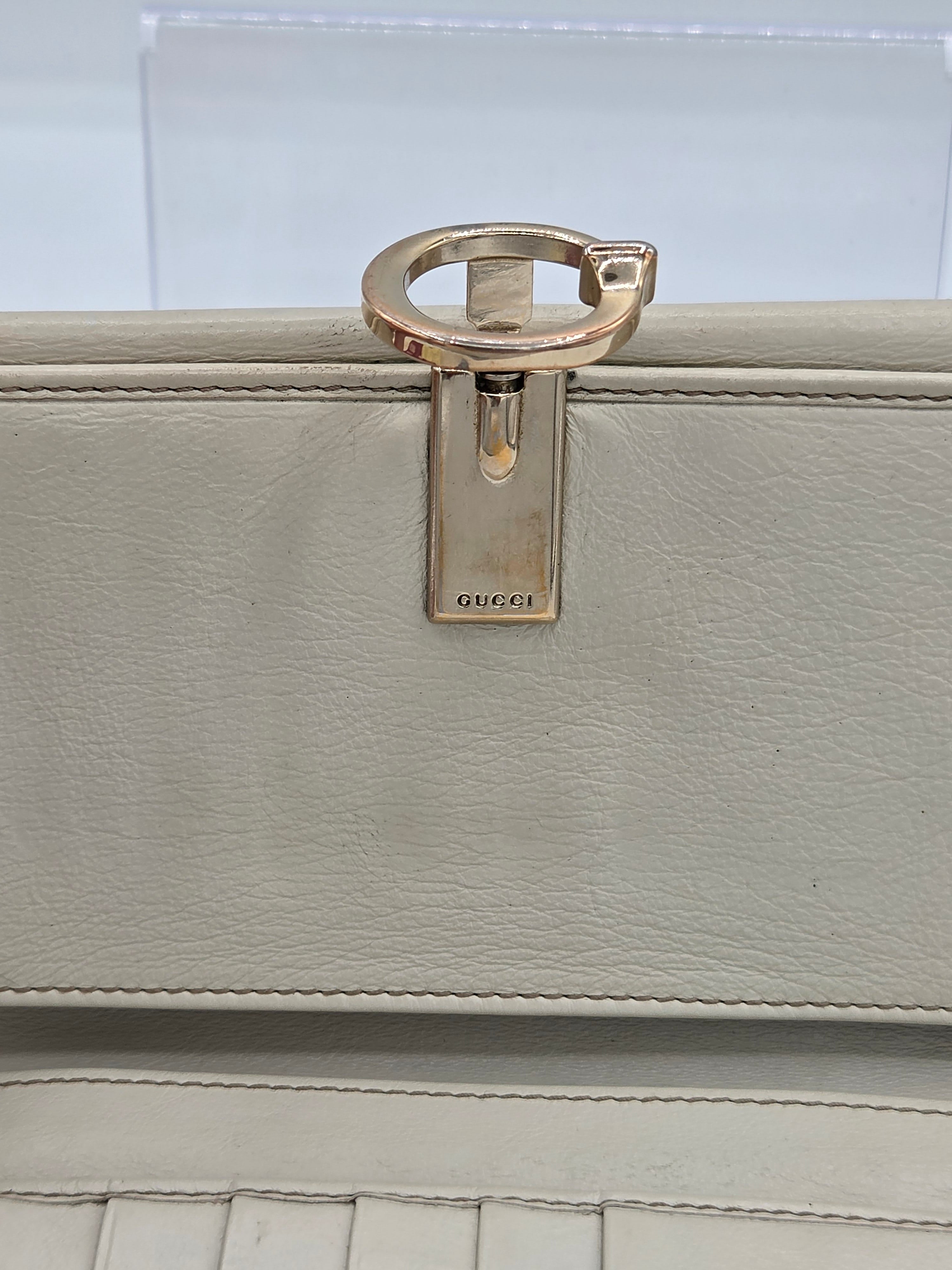 Close-up of a Gucci light beige leather bag featuring a polished gold-tone metal ring pull and a branded metal latch.