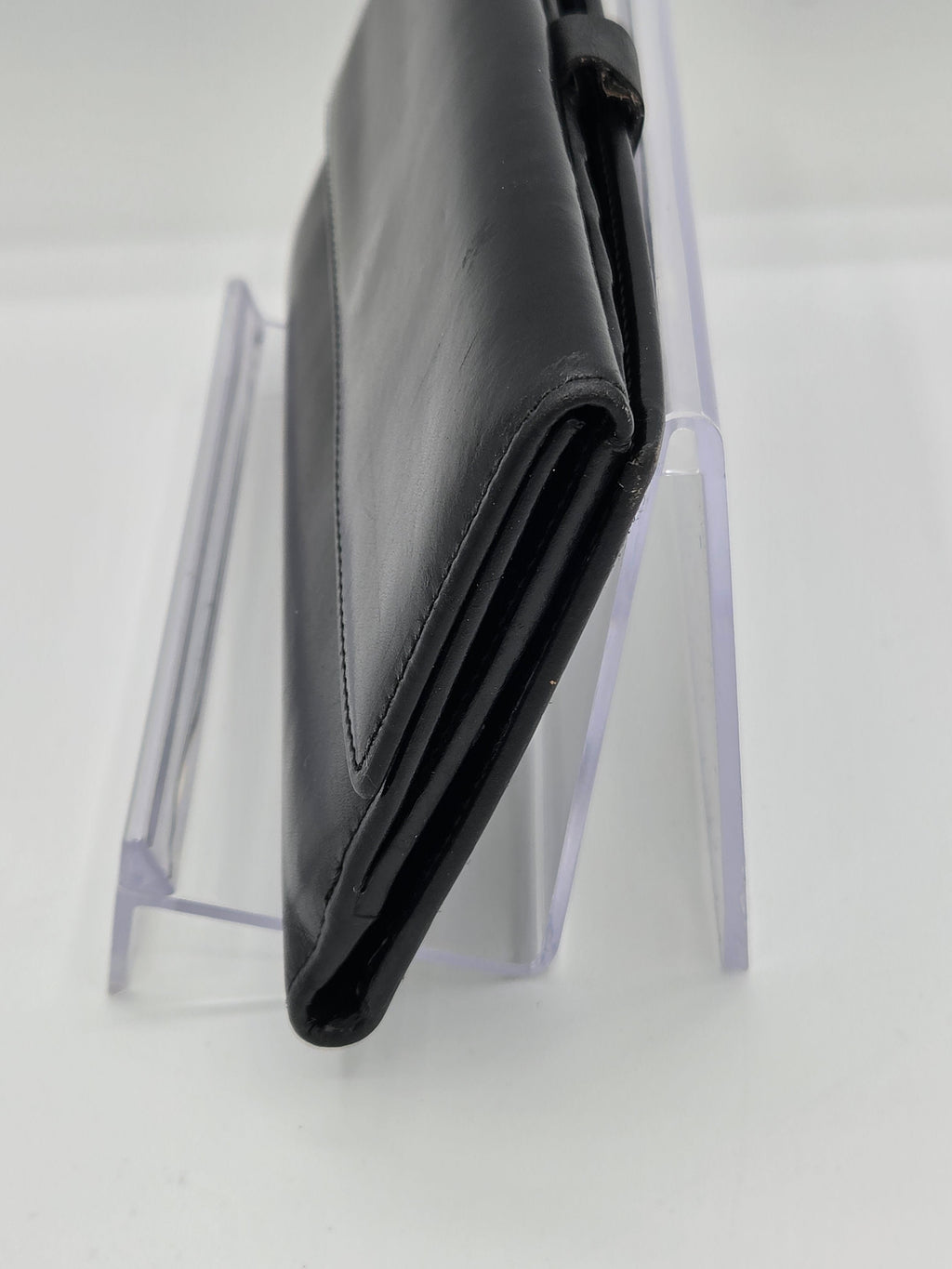 A black leather wallet or clutch standing upright on a clear acrylic display stand against a white background.