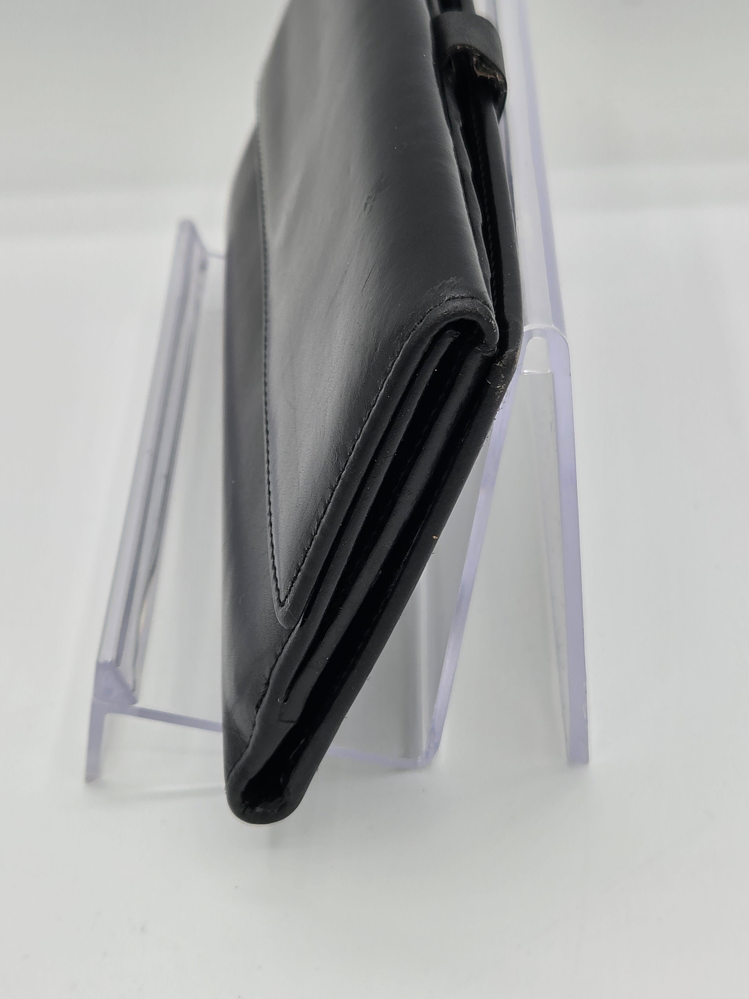 A black leather wallet or clutch standing upright on a clear acrylic display stand against a white background.