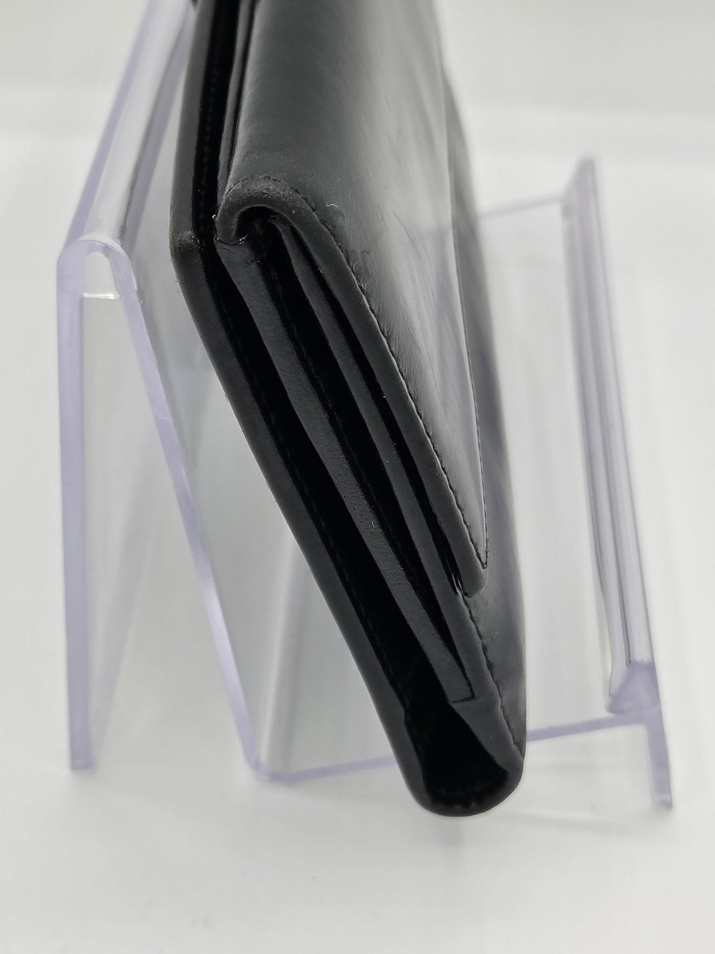 A black leather wallet standing vertically on a clear acrylic display stand against a white background.