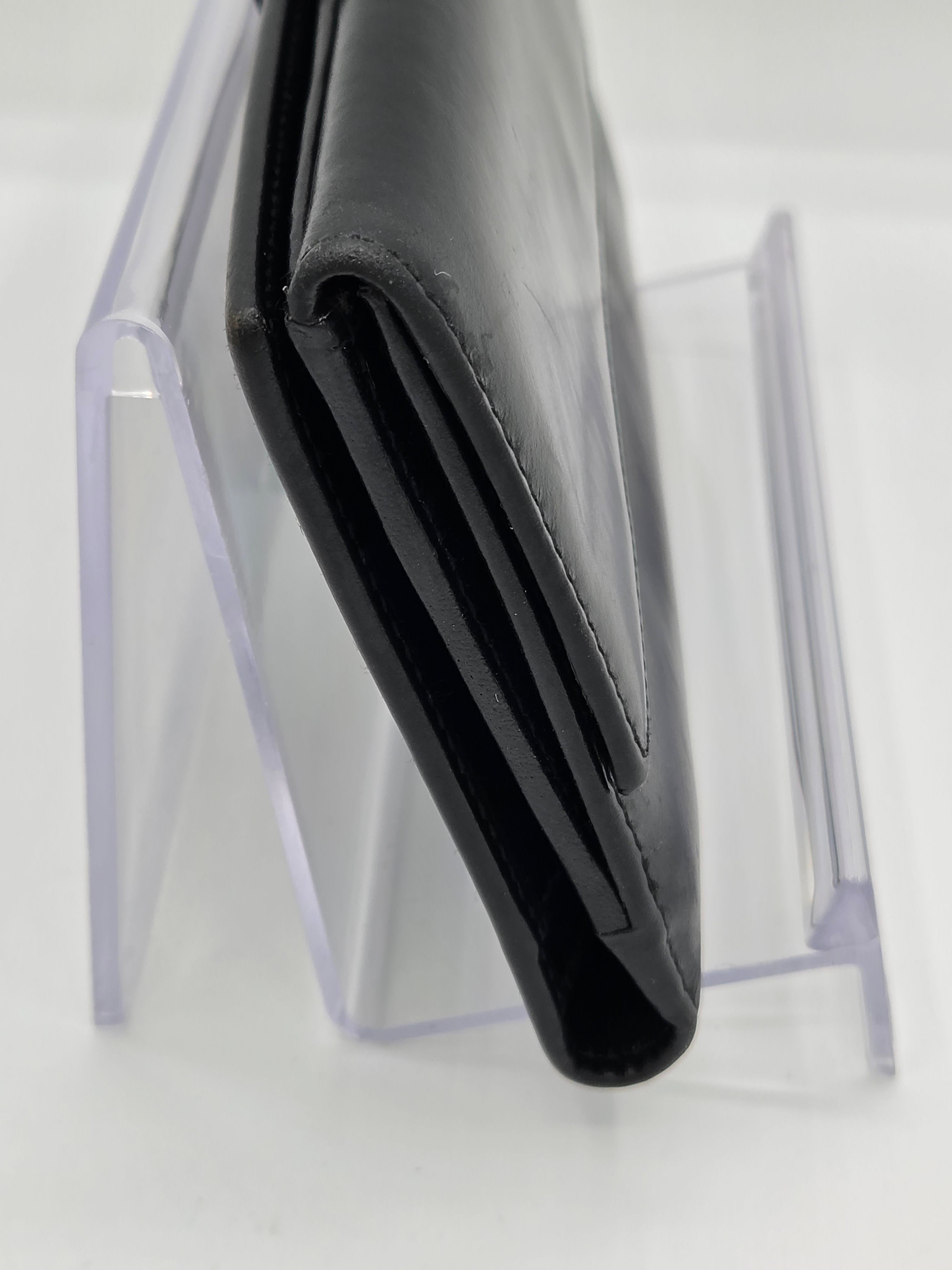 A black leather wallet standing vertically on a clear acrylic display stand against a white background.