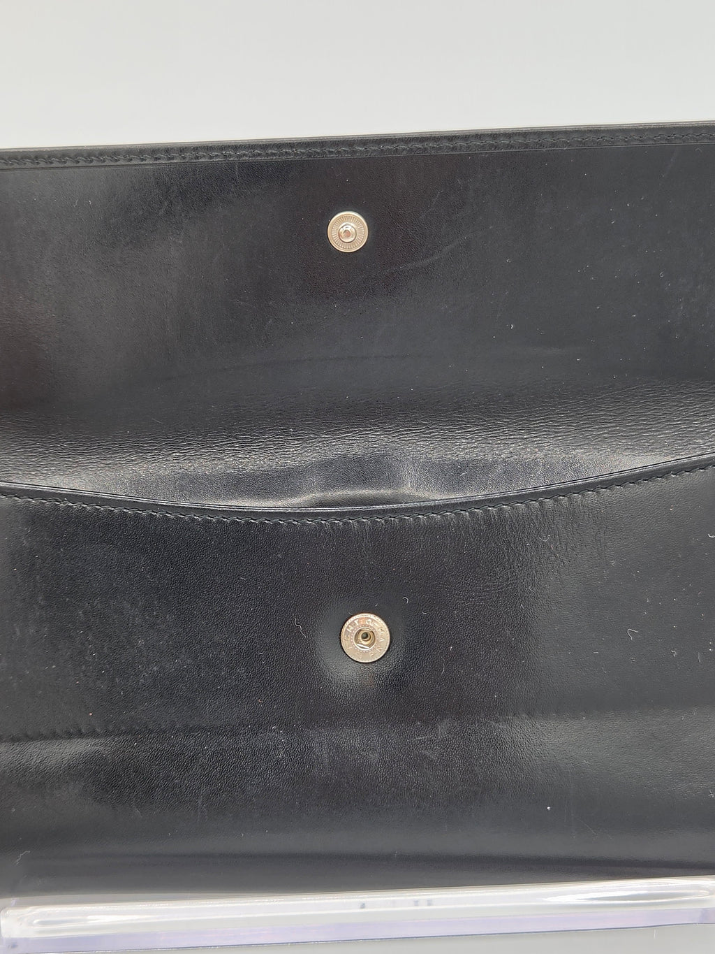 Close-up of a black leather clutch or wallet showing the interior flap with two gold-tone snap buttons.