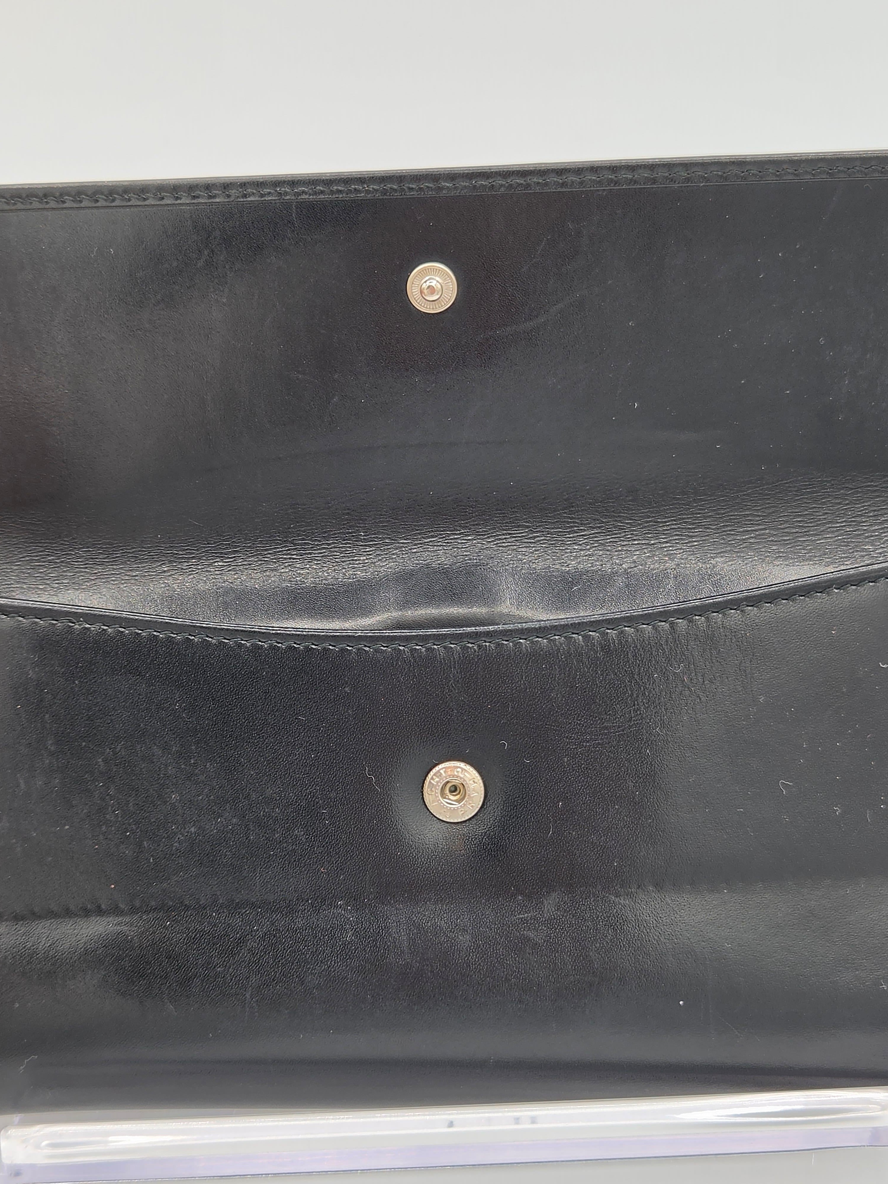 Close-up of a black leather clutch or wallet showing the interior flap with two gold-tone snap buttons.