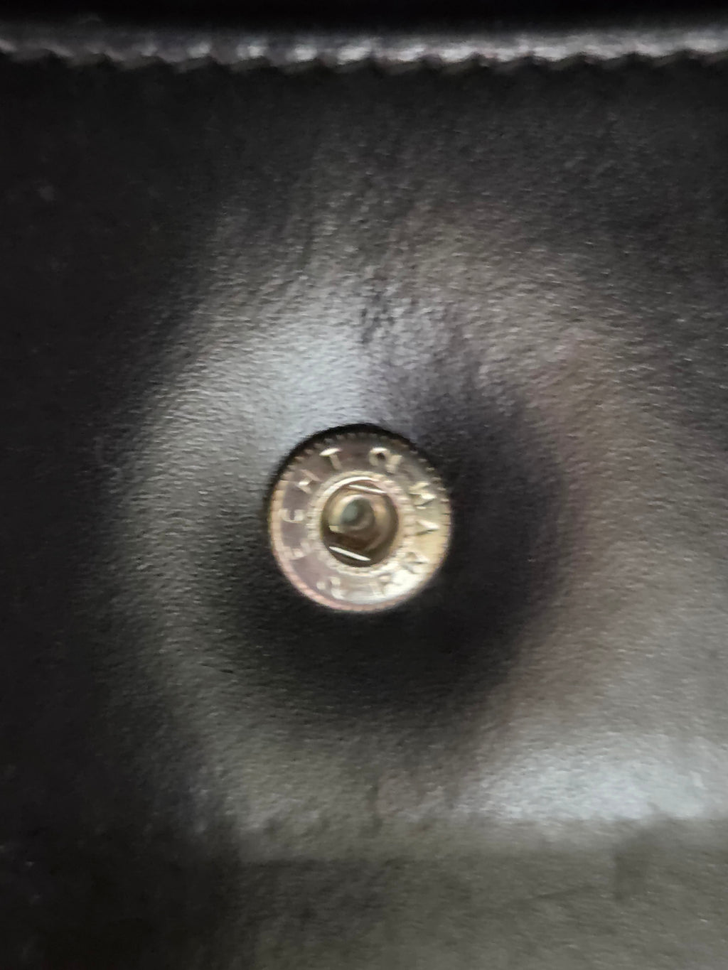 Close-up of a round metallic snap button on a black leather or faux-leather surface.