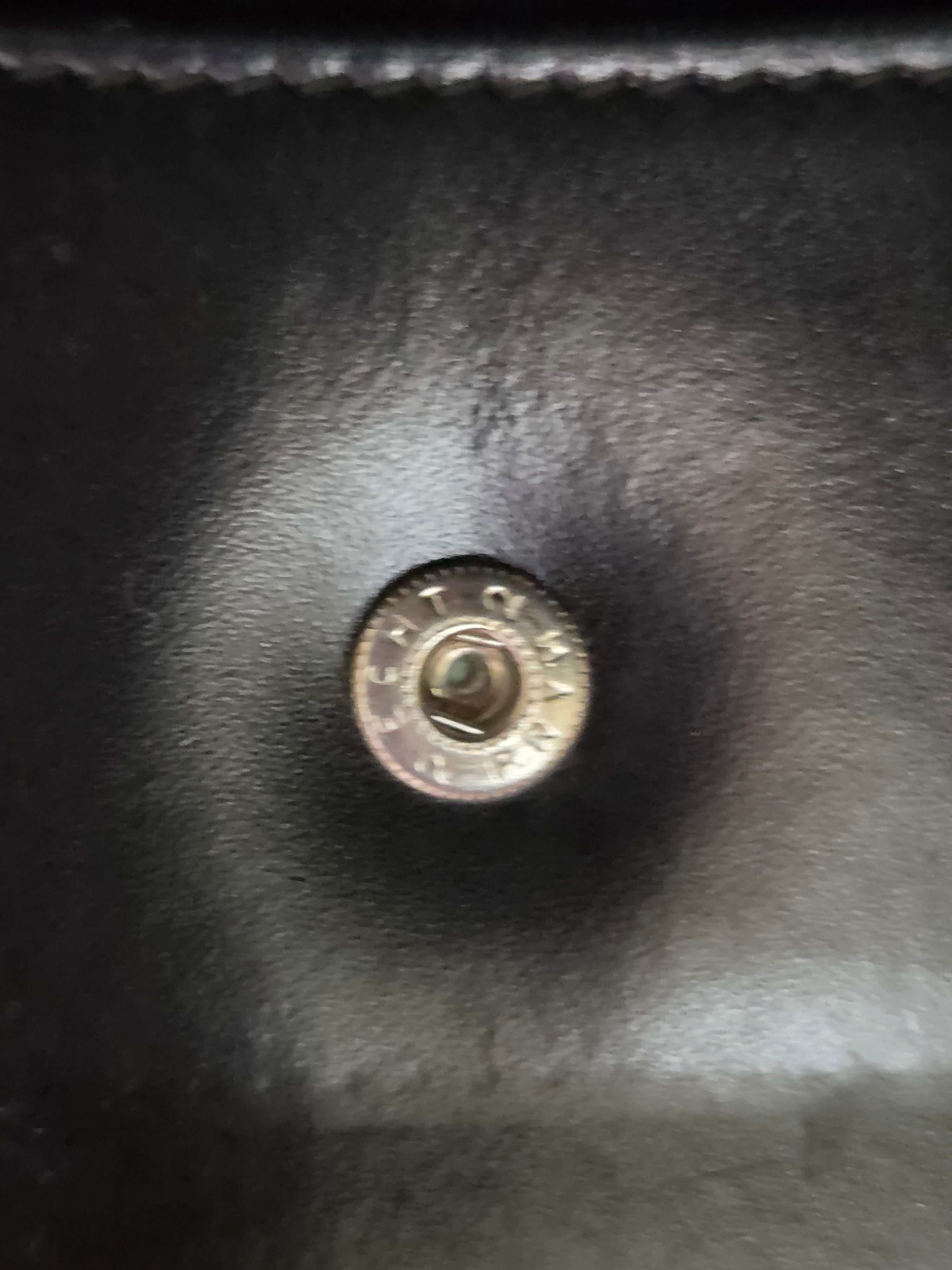 Close-up of a round metallic snap button on a black leather or faux-leather surface.