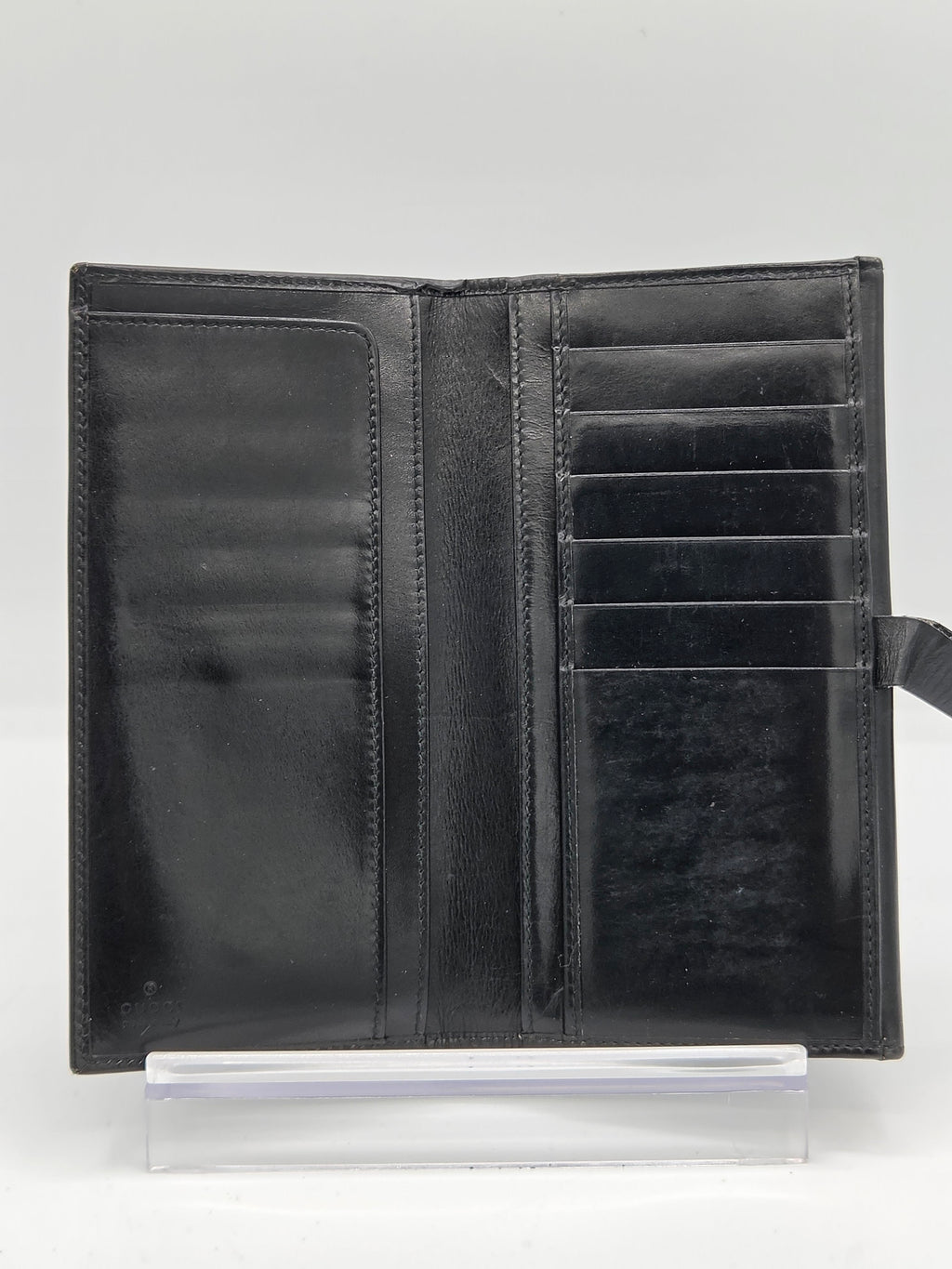 A black leather bifold wallet shown open, displaying multiple card slots and interior pockets, resting on a clear acrylic display stand against a white background.