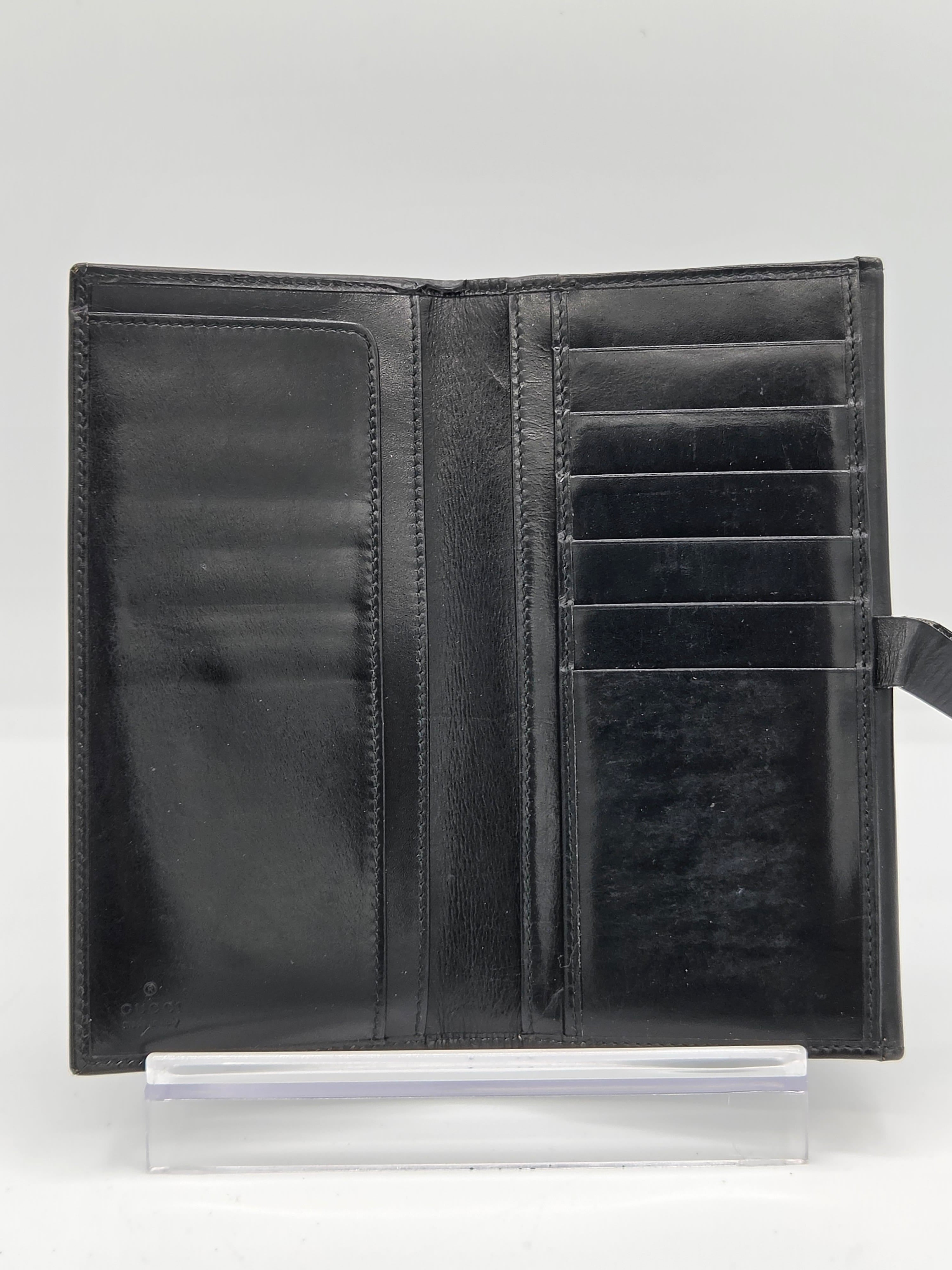 A black leather bifold wallet shown open, displaying multiple card slots and interior pockets, resting on a clear acrylic display stand against a white background.