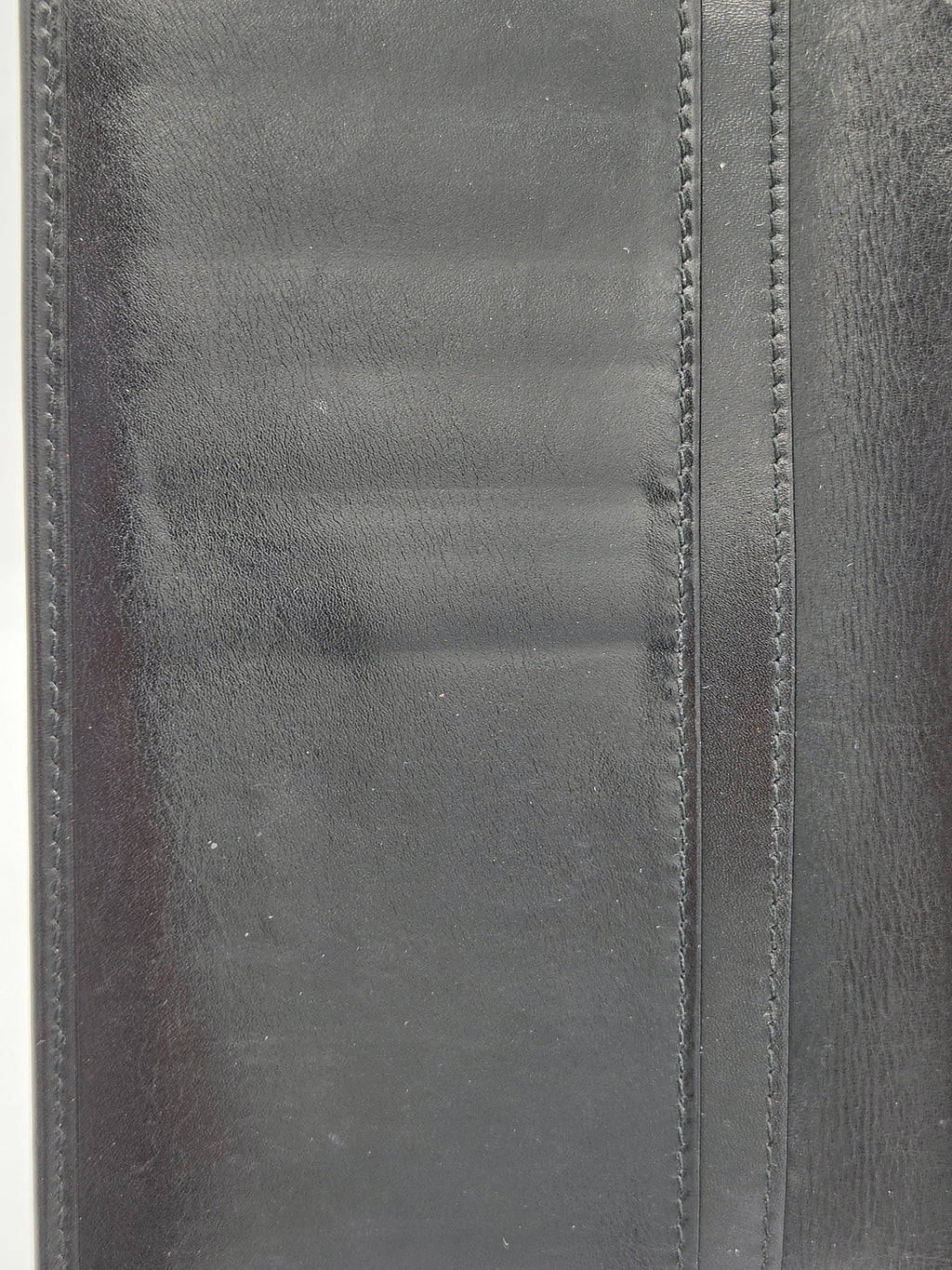 Close-up of a black leather wallet or folio showing stitched edges and a textured leather surface.