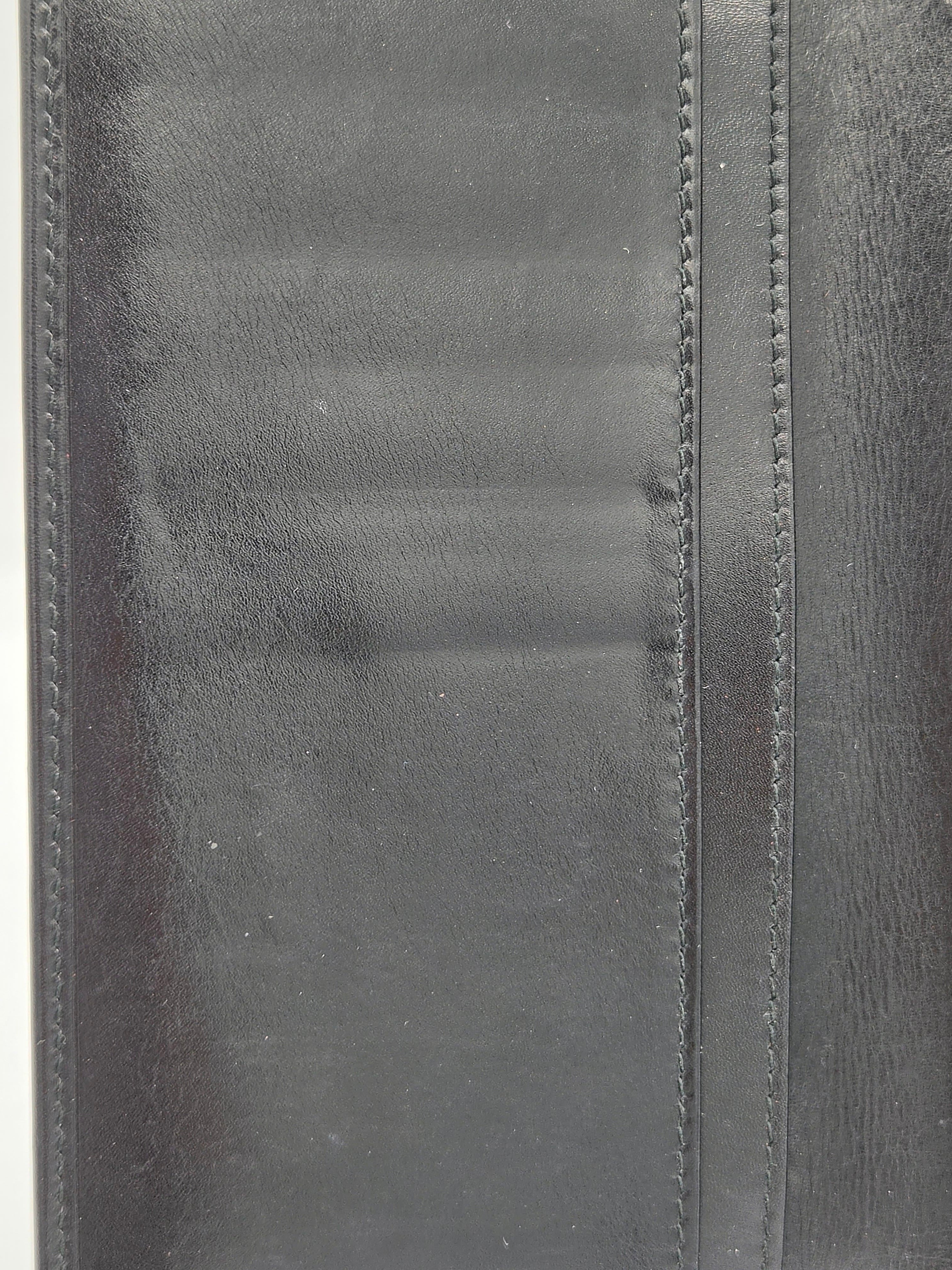 Close-up of a black leather wallet or folio showing stitched edges and a textured leather surface.