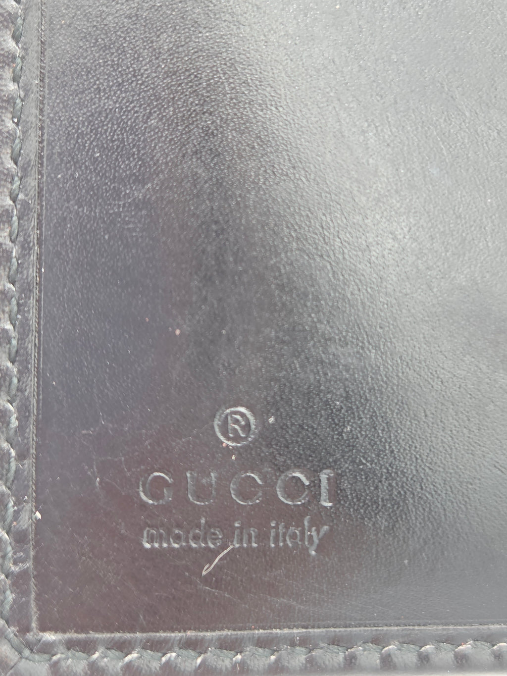 Close-up of a dark brown leather item showing the embossed Gucci logo and 'made in Italy' text on the right side, with stitched leather borders visible along the edges.