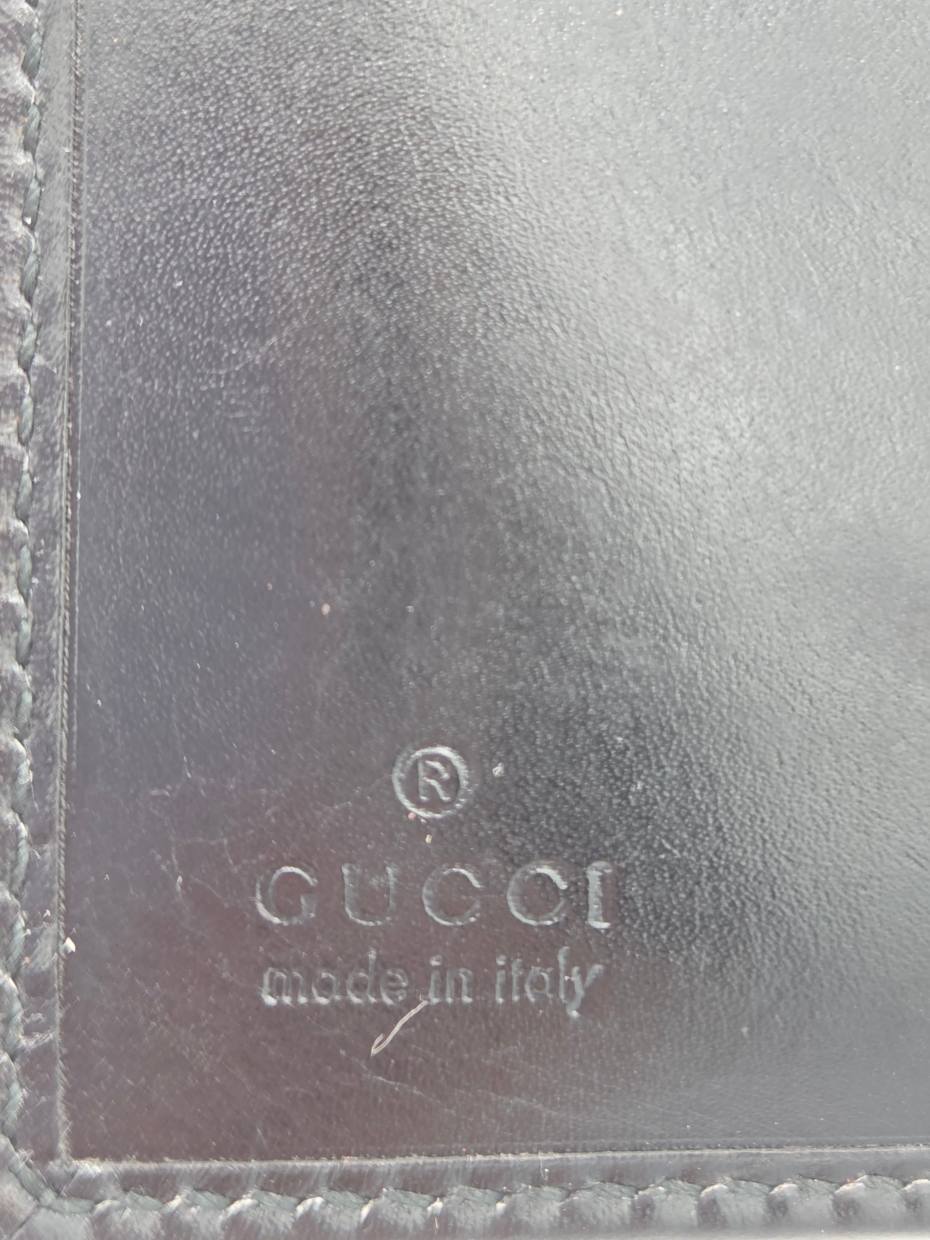 Close-up of a dark brown leather item showing the embossed Gucci logo and 'made in Italy' text on the right side, with stitched leather borders visible along the edges.