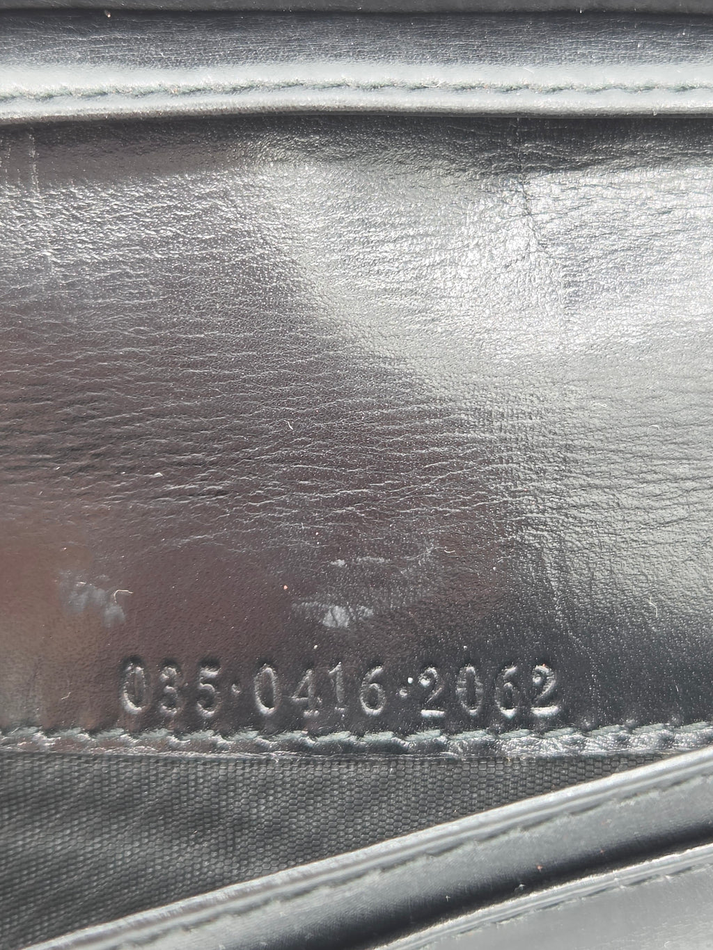 Close-up of a black leather product surface with visible grain, stitching, and embossed serial numbers near the bottom.