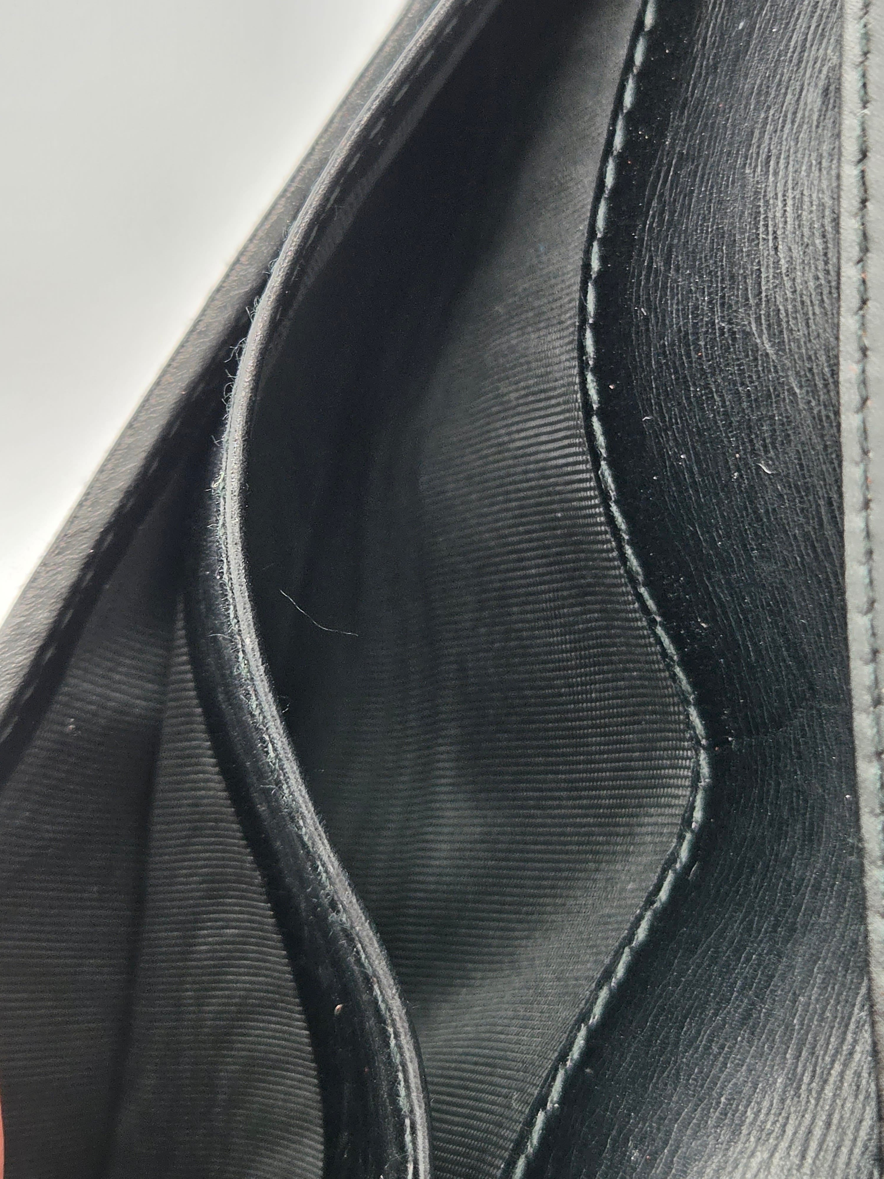 Close-up of the interior lining of a black leather or faux-leather pouch or wallet, showing stitched edges and a dark fabric lining.