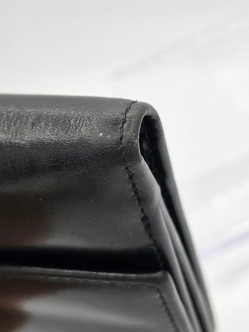 Close-up detail shot of a black leather wallet corner showing the texture of the leather and the stitching.