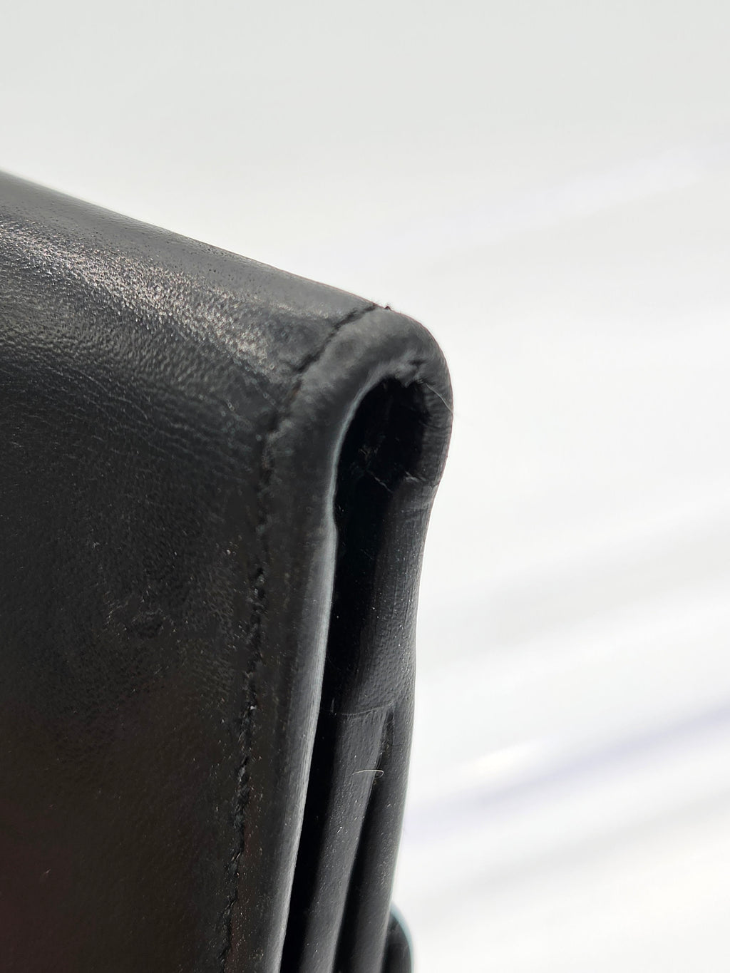 Close-up of a black leather wallet corner showing the texture of the leather and a stitched edge against a white background.