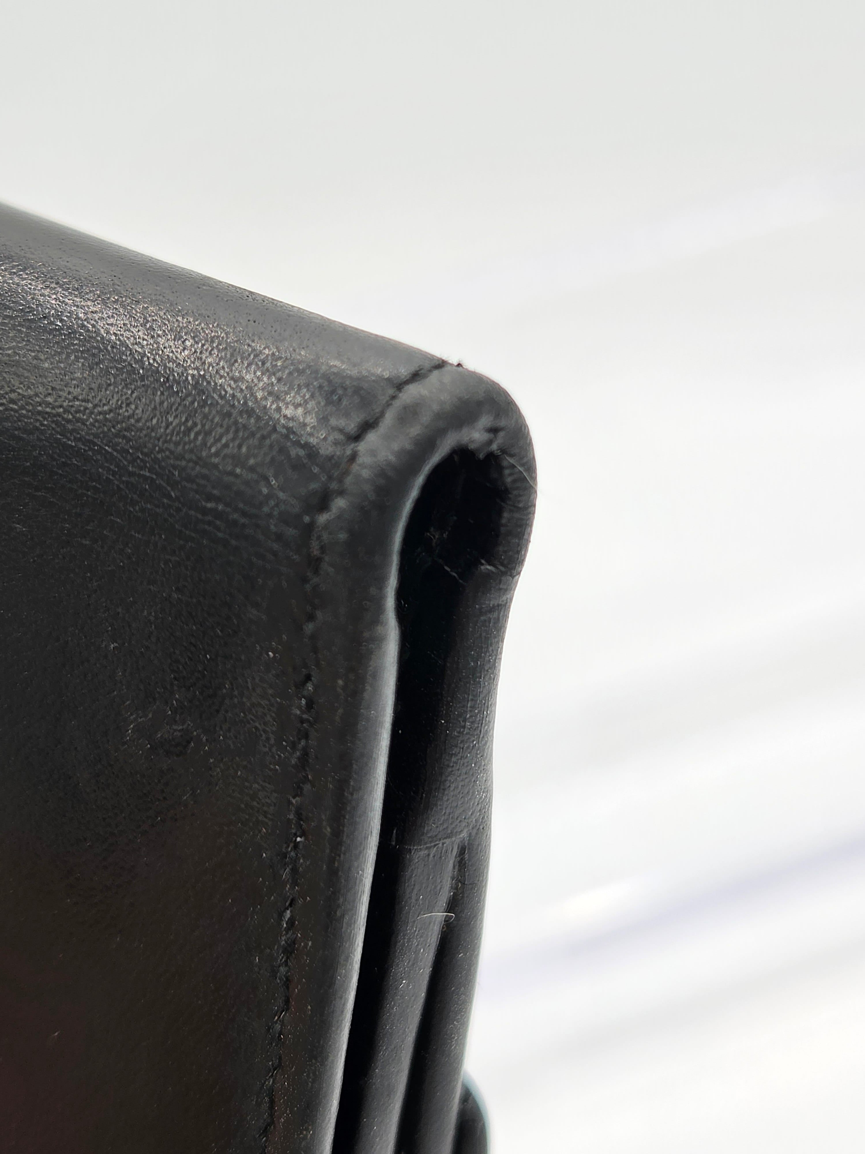 Close-up of a black leather wallet corner showing the texture of the leather and a stitched edge against a white background.