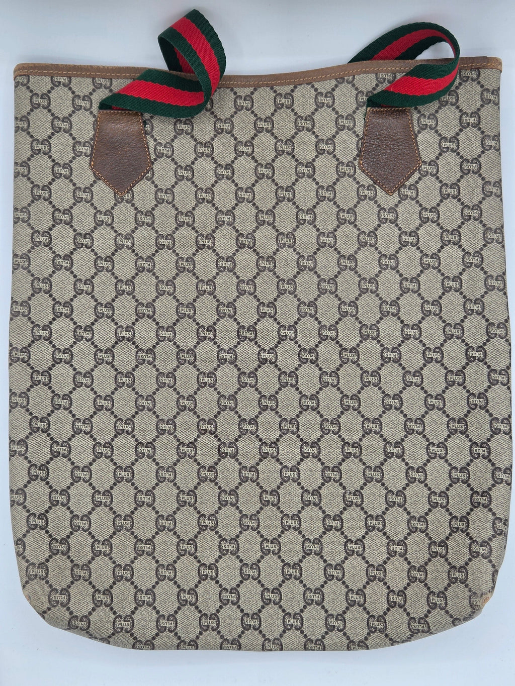 A Gucci canvas tote bag featuring the signature GG monogram pattern in beige and brown, with green and red web stripe accents on the handles and brown leather trim.