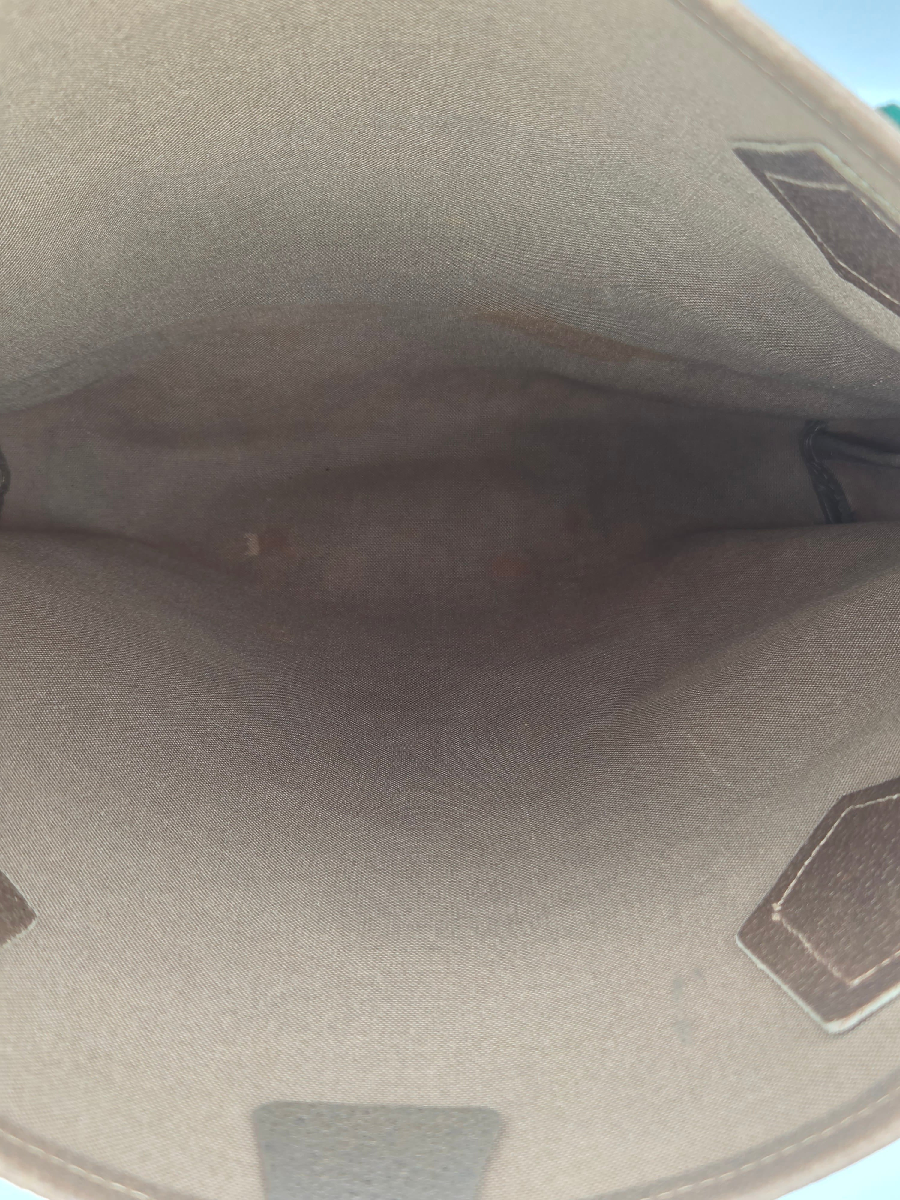 Close-up view of the interior lining of a beige or taupe bag, showing a textured fabric surface with dark brown stitched geometric accents.