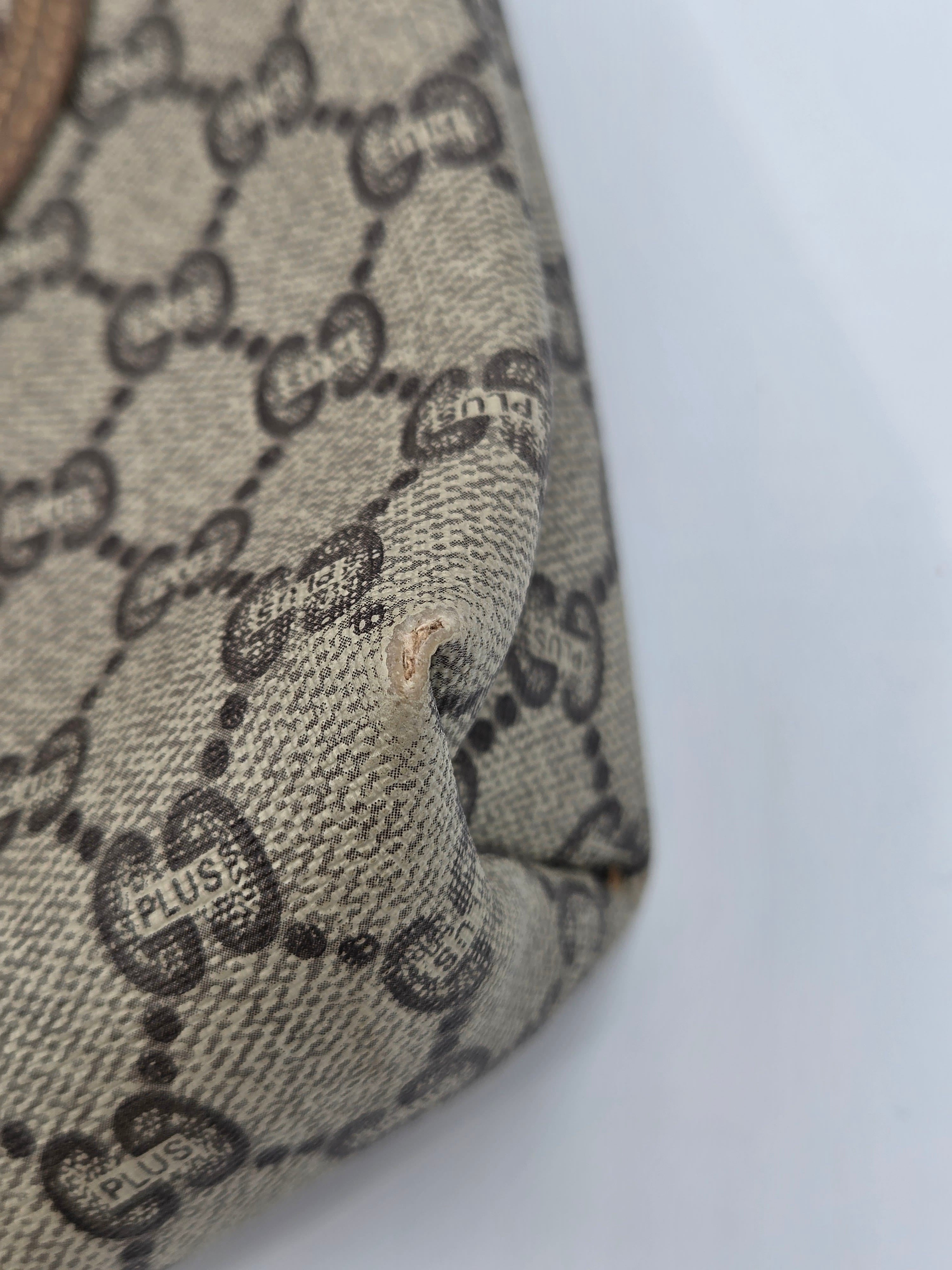 Close-up of a beige and brown Gucci monogram canvas material with visible wear and a small hole near the center.