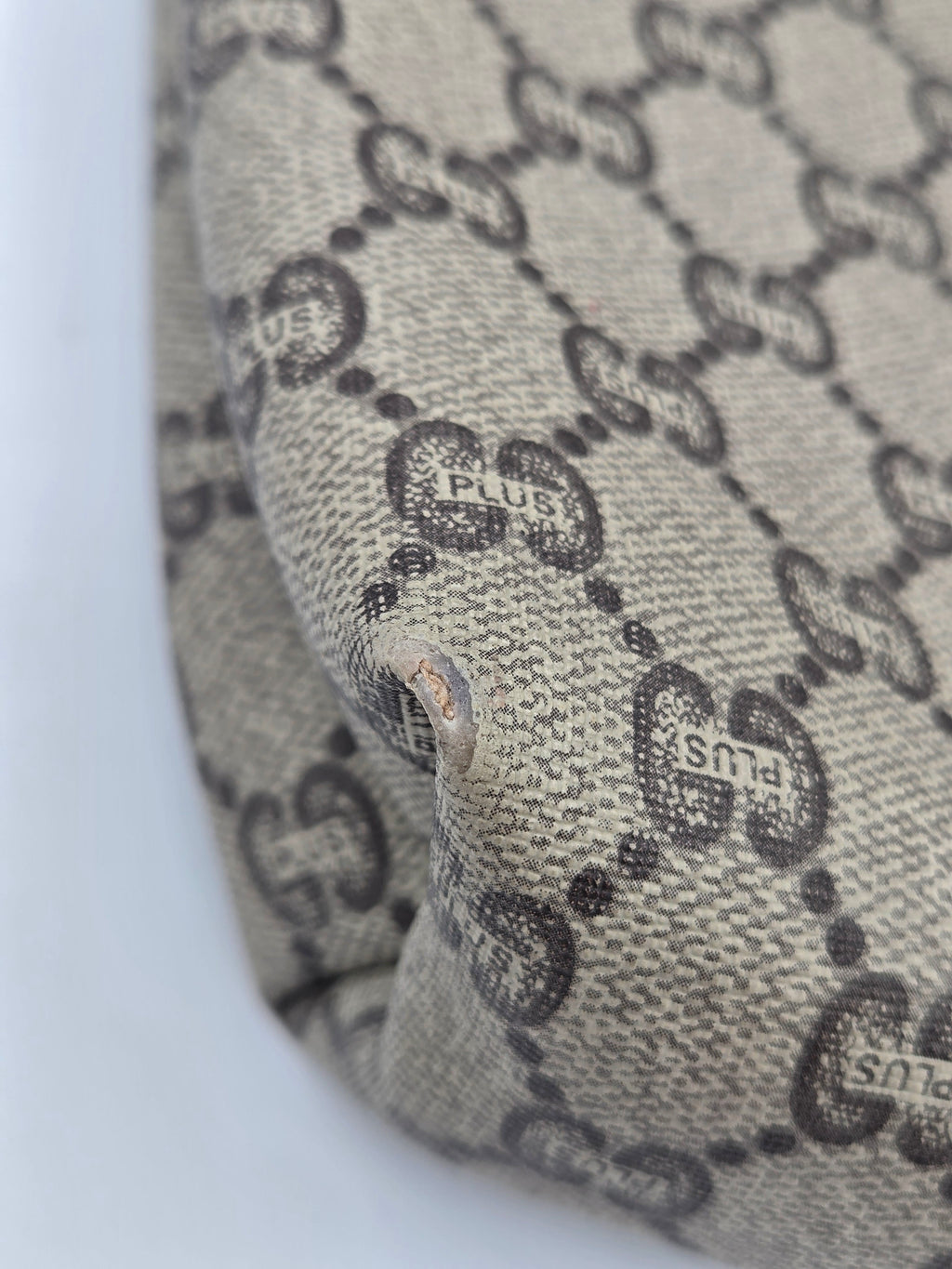 Close-up of a beige canvas material with a dark brown interlocking GG monogram pattern, showing a small metal rivet detail.