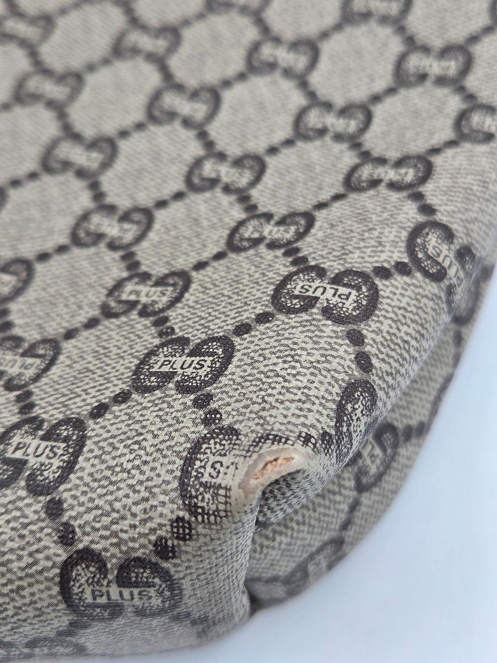 Close-up of a beige and black monogram fabric with a visible hole and frayed edge, showing the repeating interlocking GG pattern.