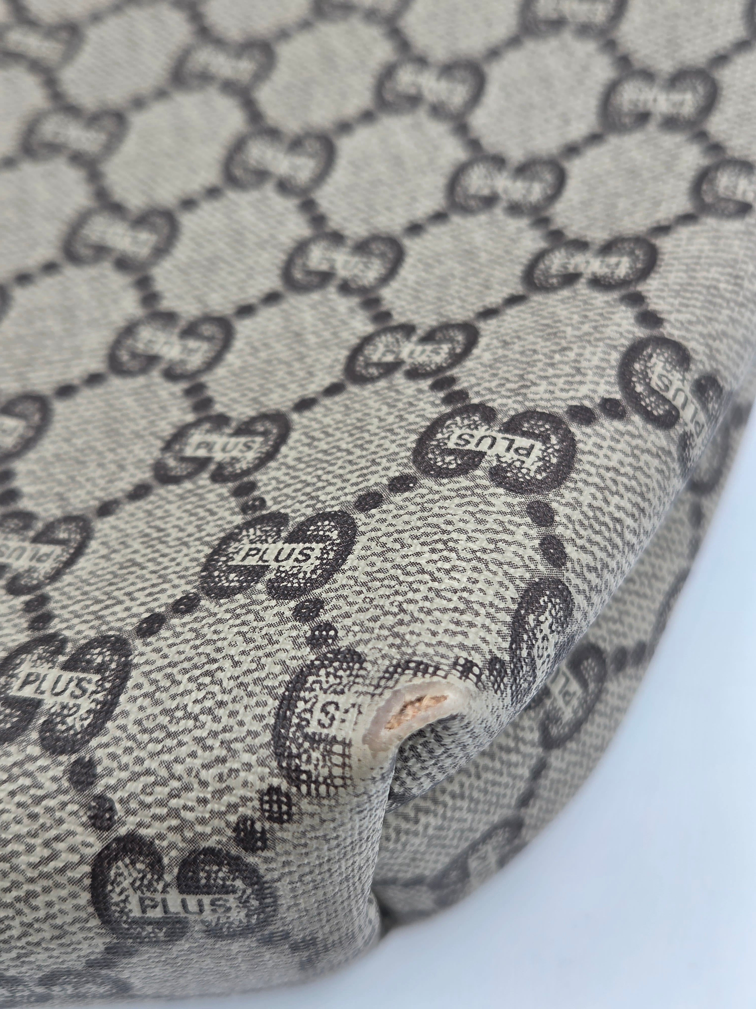 Close-up of a beige and black monogram fabric with a visible hole and frayed edge, showing the repeating interlocking GG pattern.
