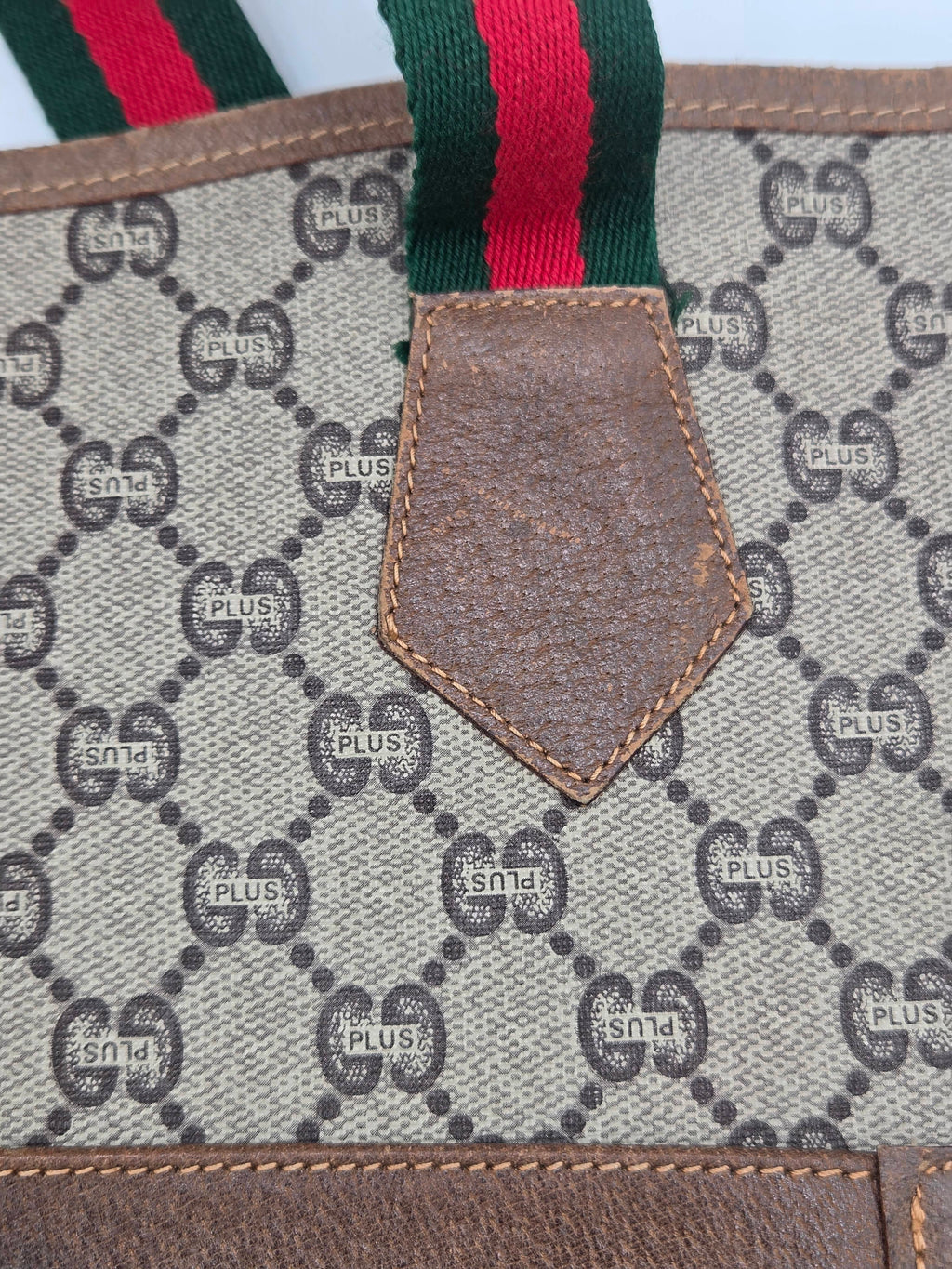 Close-up of a Gucci monogram canvas bag with brown leather trim and a green and red web stripe detail.